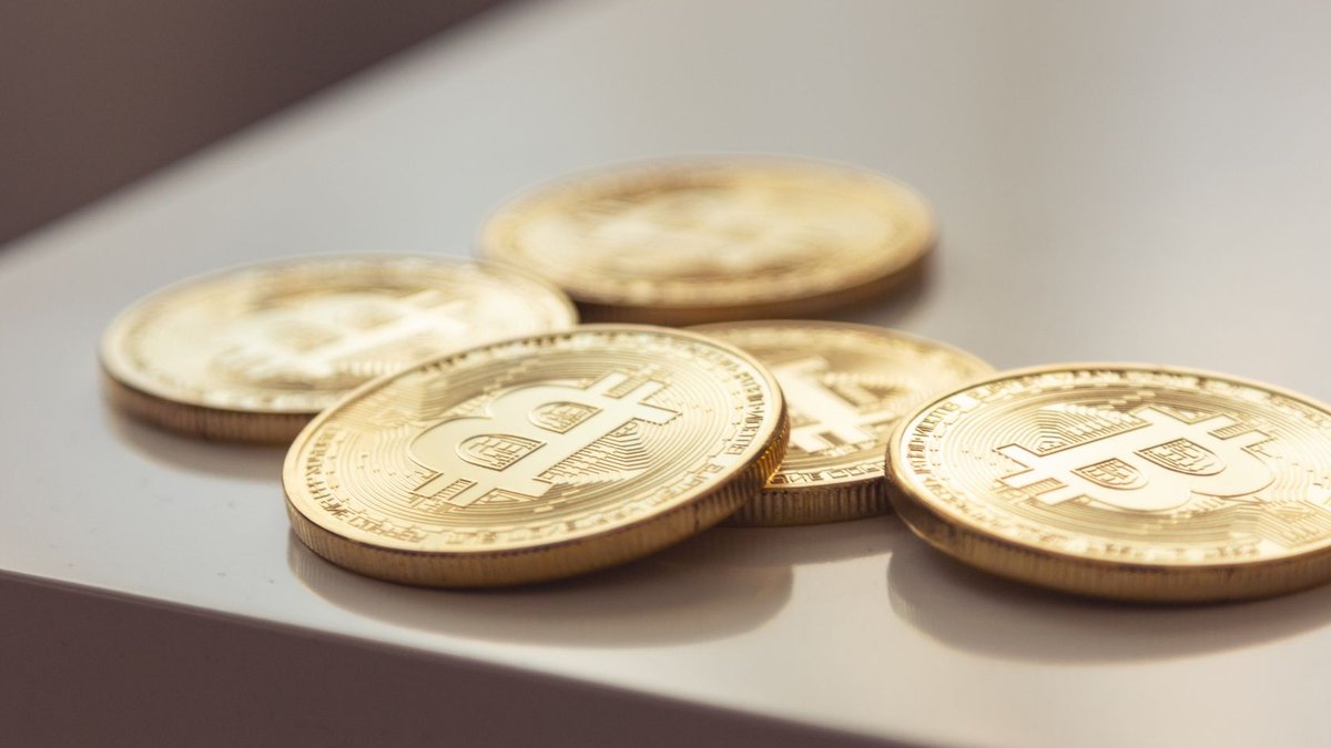 OTC Markets to host virtual investor conference on digital assets Close-up of shiny gold Bitcoin coins on white surface, symbolizing cryptocurrency wealth.