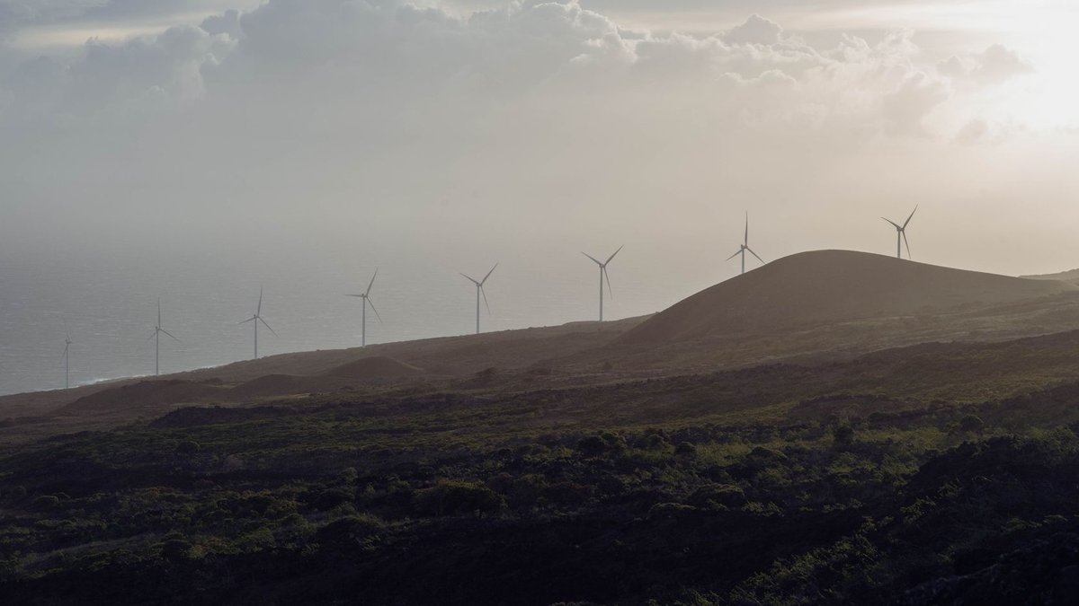 Wind turbines spin on hills under a cloudy sky, creating an eco-friendly energy source.