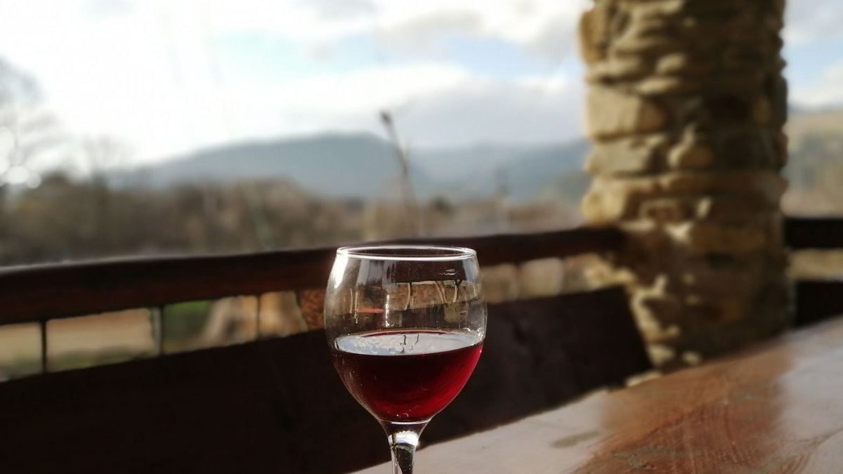 Ocado adds lower alcohol wine range A peaceful outdoor setting with a glass of red wine on a wooden table.