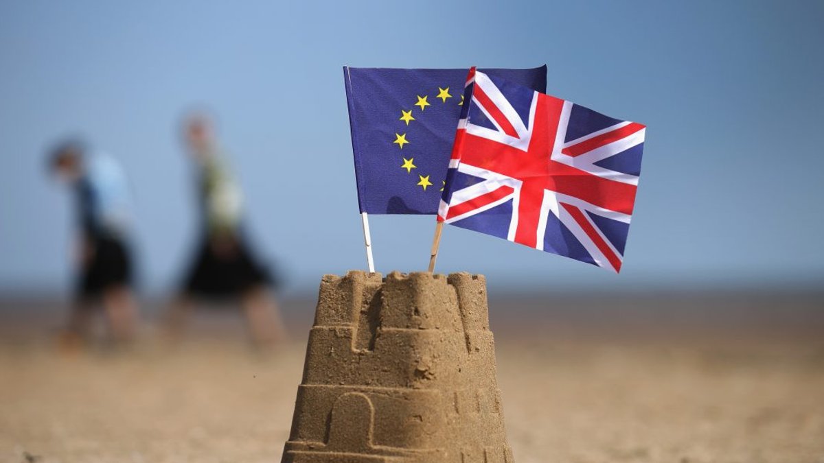 UK and EU flags planted in a sandcastle on a beach, symbolizing Brexit negotiations.