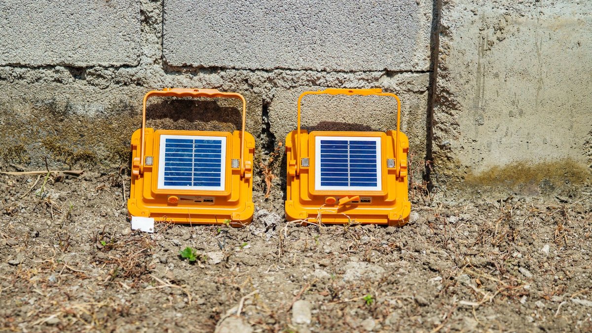 Two orange portable solar lamps placed on the ground against a concrete wall, absorbing sunlight.