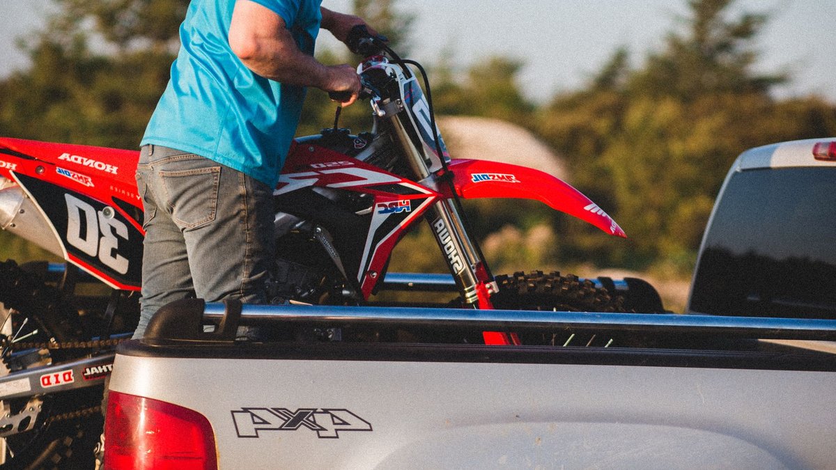 A man in blue loads a Honda motorcycle into a pickup truck at sunset, outdoors.