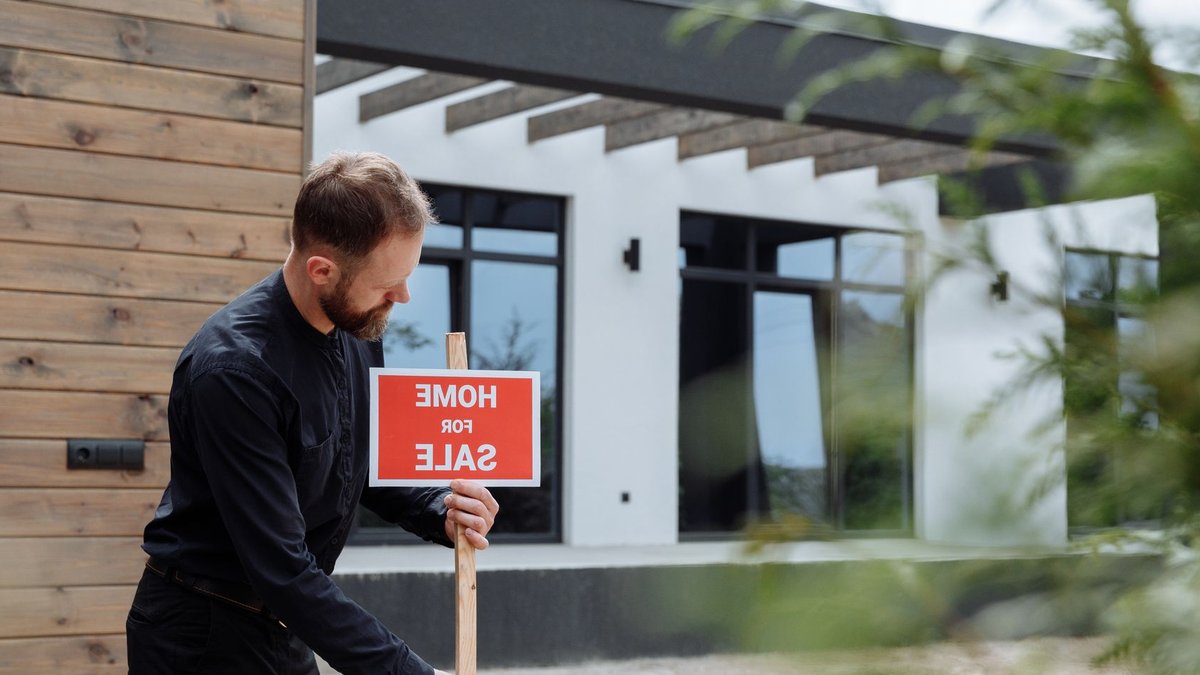 Coming-soon homes sell for more than private or standard listings Man placing a home for sale sign outside a modern house for real estate listing.