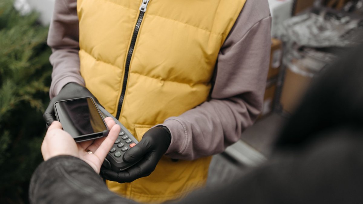 NMI expands business capital program for merchants Outdoor delivery person processing contactless payment with a smartphone and terminal.