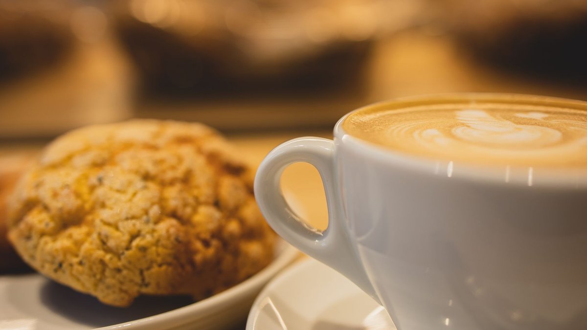 La Madeleine launches new coffee program nationwide Mug of tasty fragrant coffee with latte art served near plate with oatmeal cookies on table on blurred background.