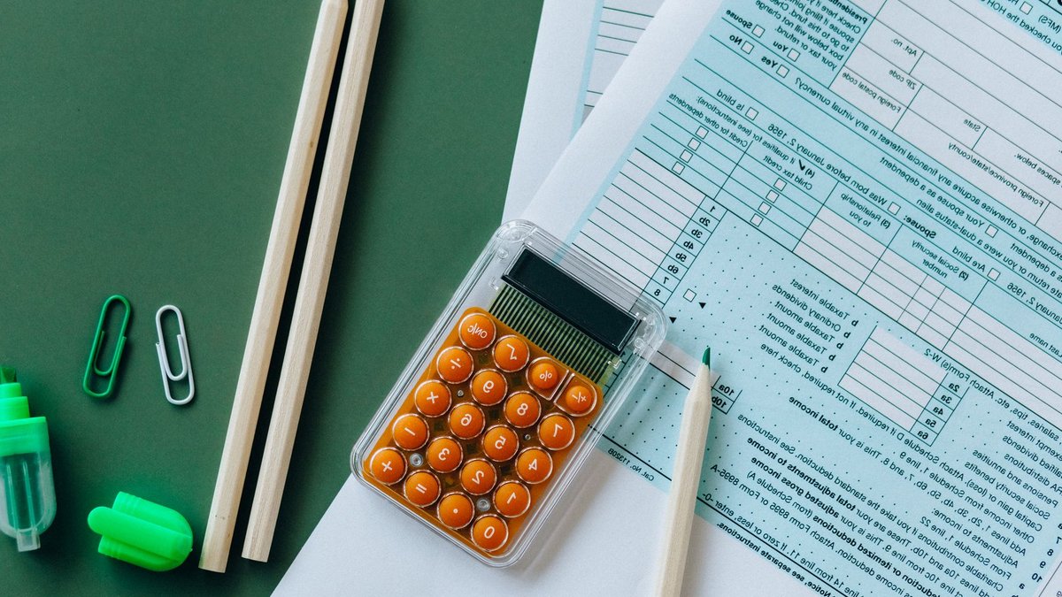 Flat lay of tax forms, calculator, pencils, and clips on green surface, ideal for finance or accounting themes.