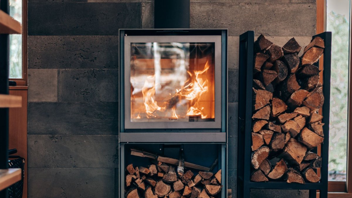 Choosing the right stove fuel type Contemporary square fireplace with burning flame and fuel woods stand located in stylish modern cottage.