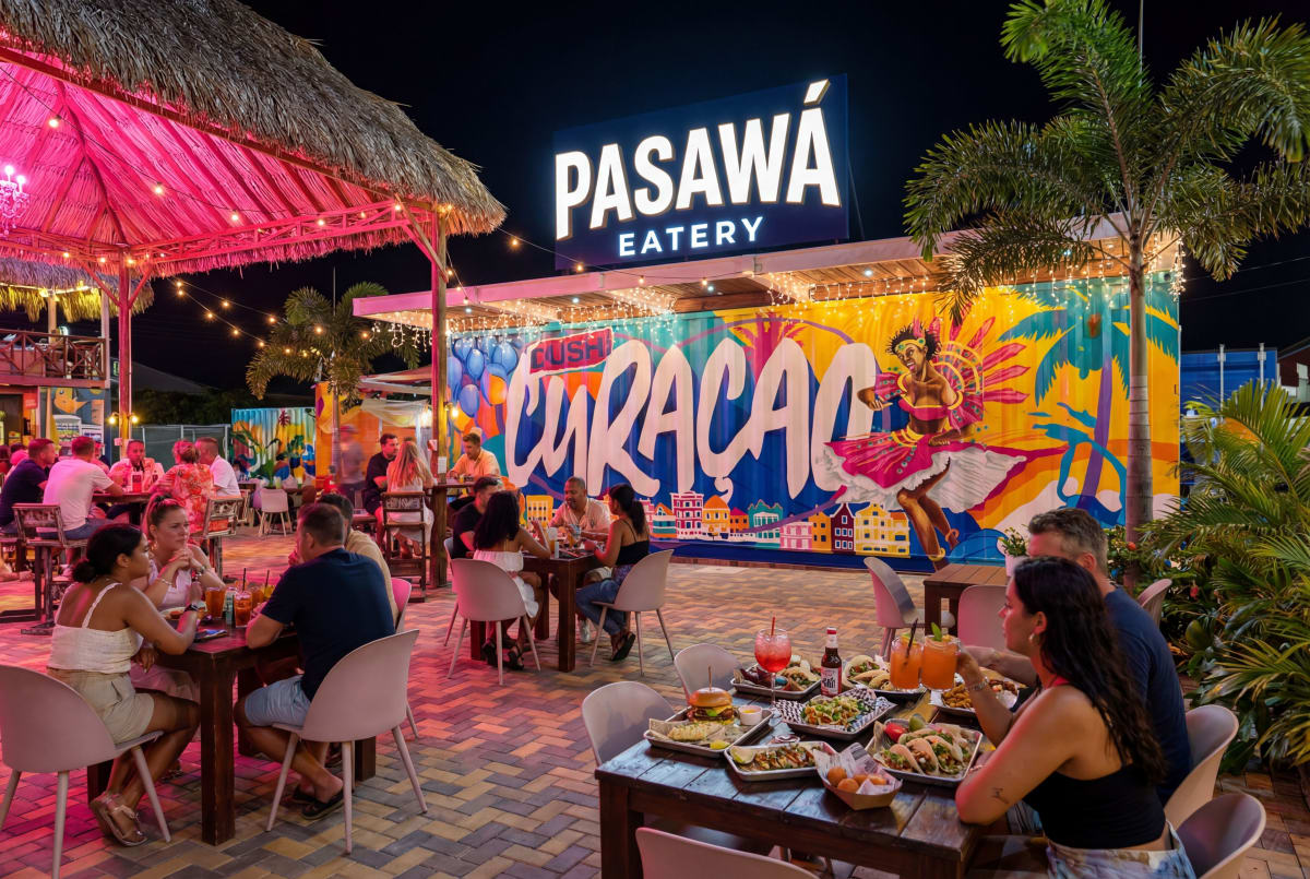 An evening at Pasawa Eatery, with guests dining beneath the palms and Curaçao mural.