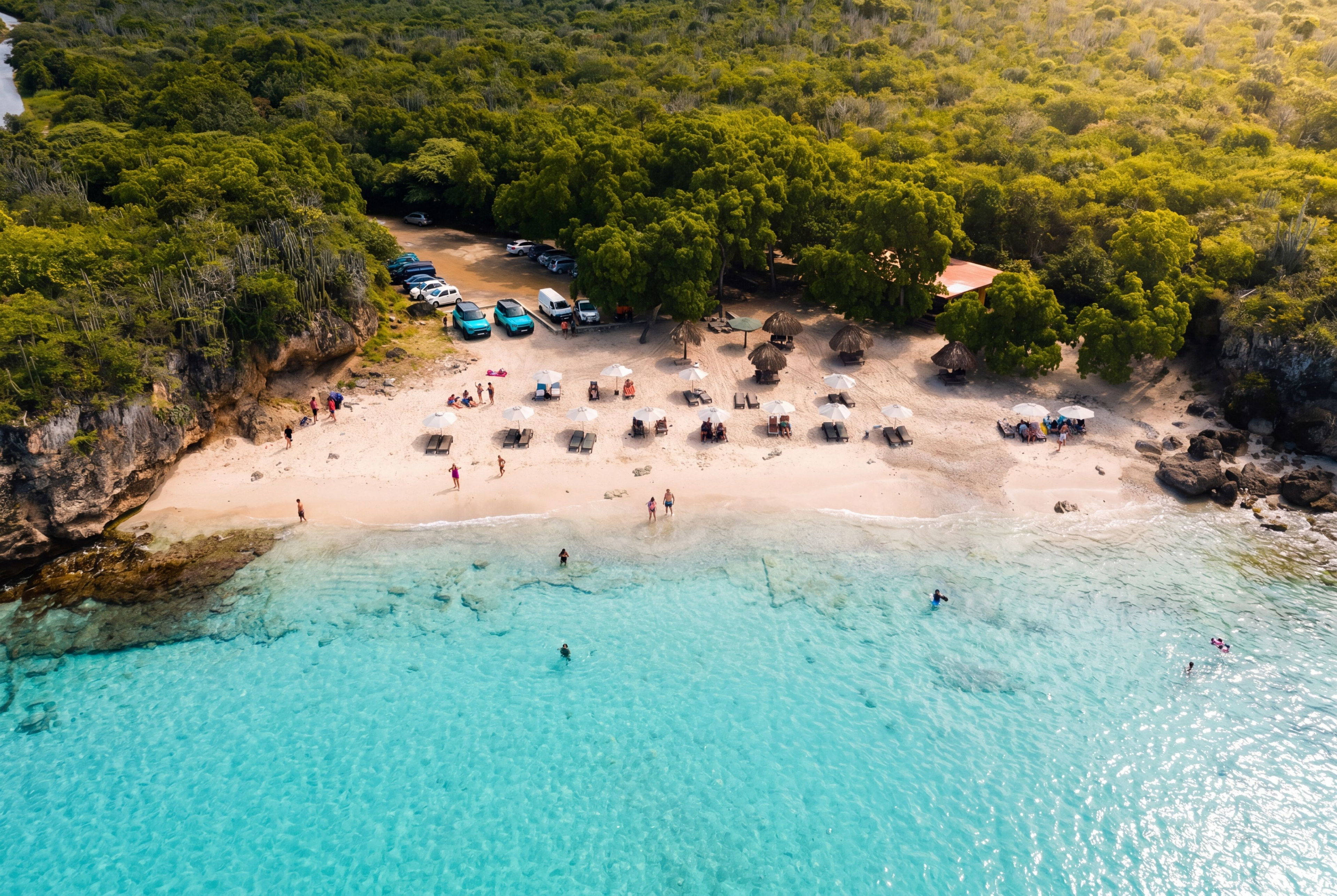 Kleine Knip at midday — entirely empty, two snorkelers, palms and cliffs framing the cove