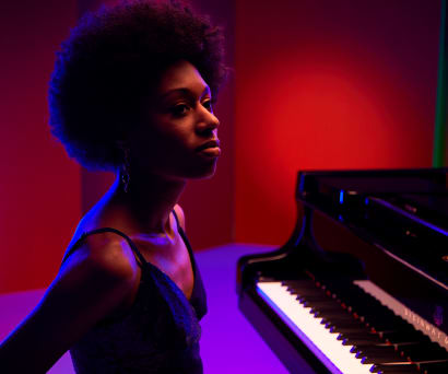 Isata Kanneh-Mason sitting at a grand piano against red and blue lighting