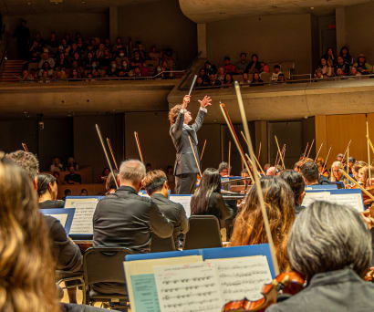 Gustavo Gimeno conducting the orchestra with his arms raised.