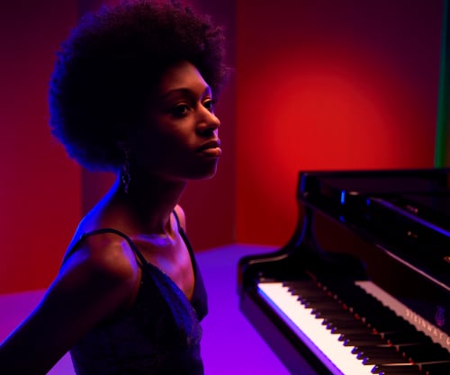 Isata Kanneh-Mason sitting at a grand piano against red and blue lighting