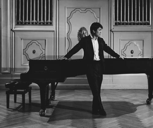 Black and white photo of Seong-Jin Cho standing infront of a grand piano