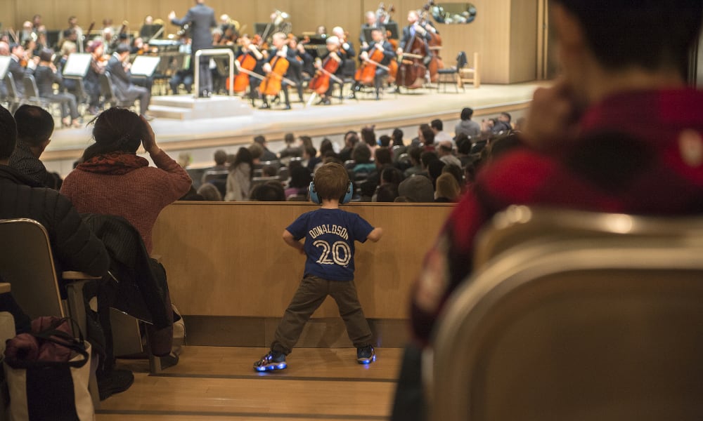 Young child standing in the aisle watching the performance with a noise cancelling headset on.