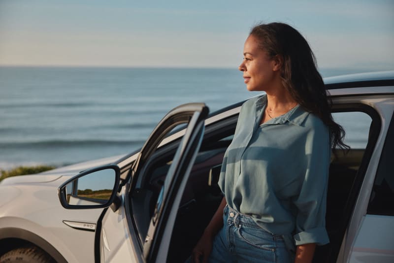 Woman standing outside car door looking out by the sea