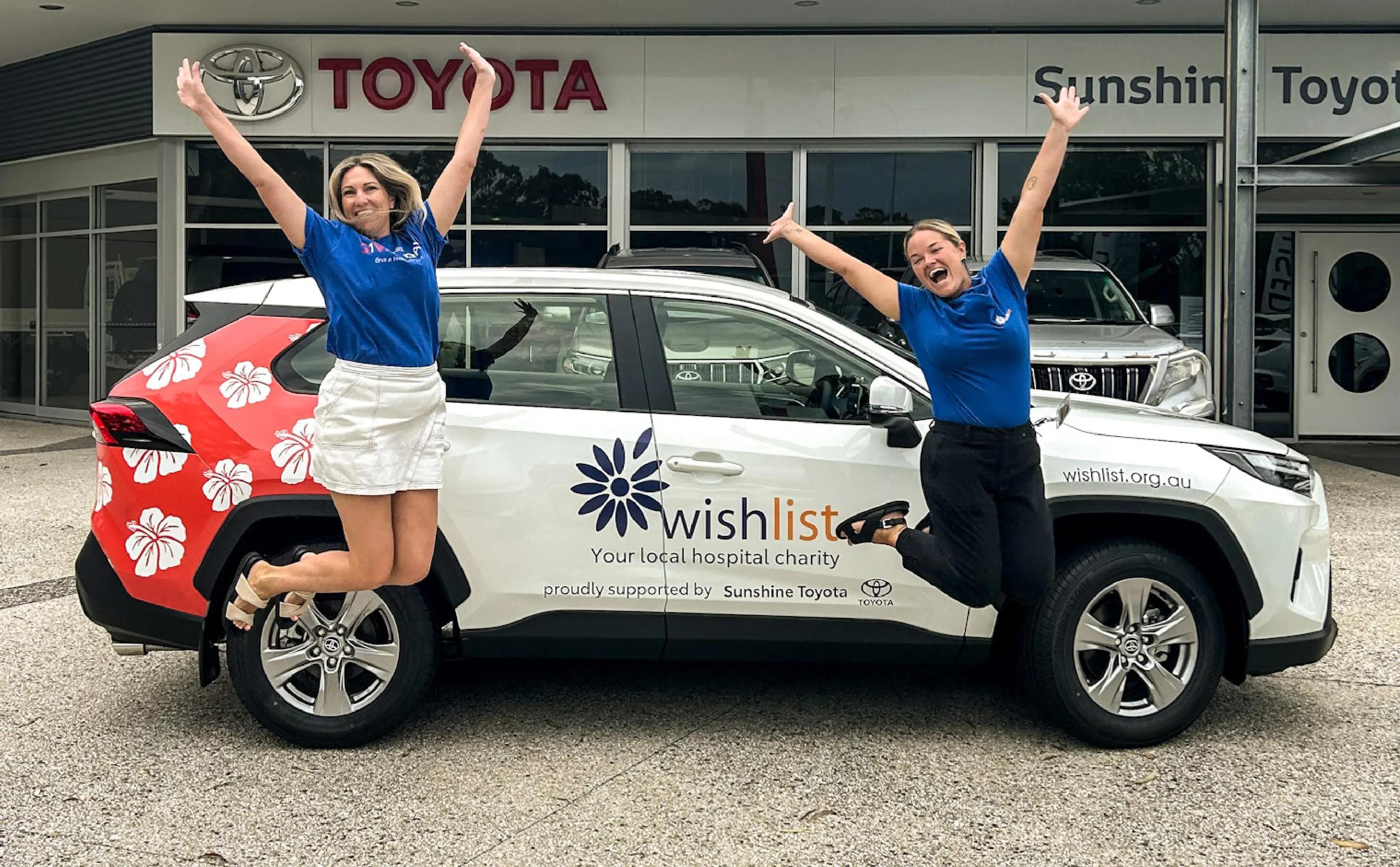 2 people jumping next to wishlist car at sunshine toyota