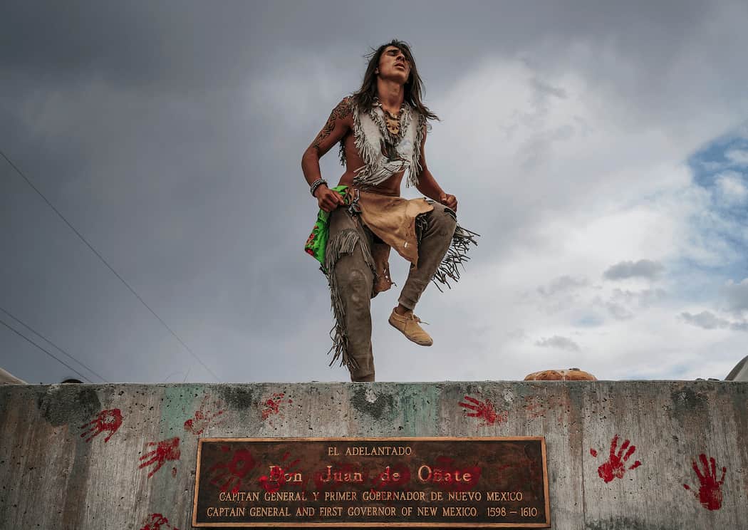 a photo of Than Tsideh, of Ohkay Owingeh Pueblo dancing on the empty platform of a statue of Juan de Oñate