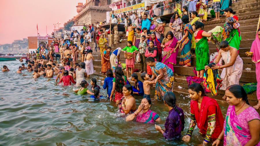 Showing the colorful traditional clothing and Hindu religious ritual of bathing in the Ganges River from the ancient ghats of Varanasi.