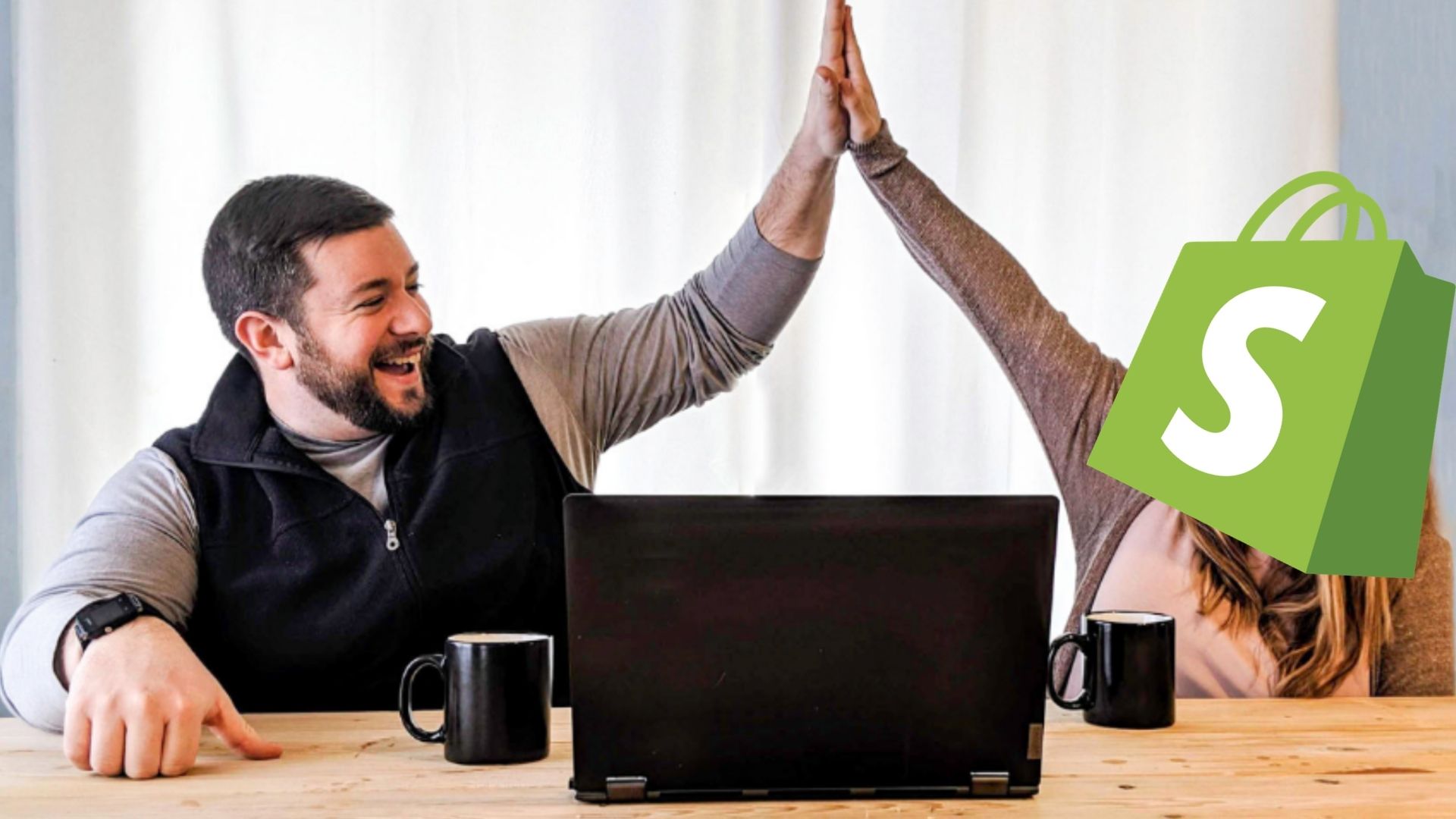 man hi-fiving another person with shopify logo over their face in front of a laptop computer