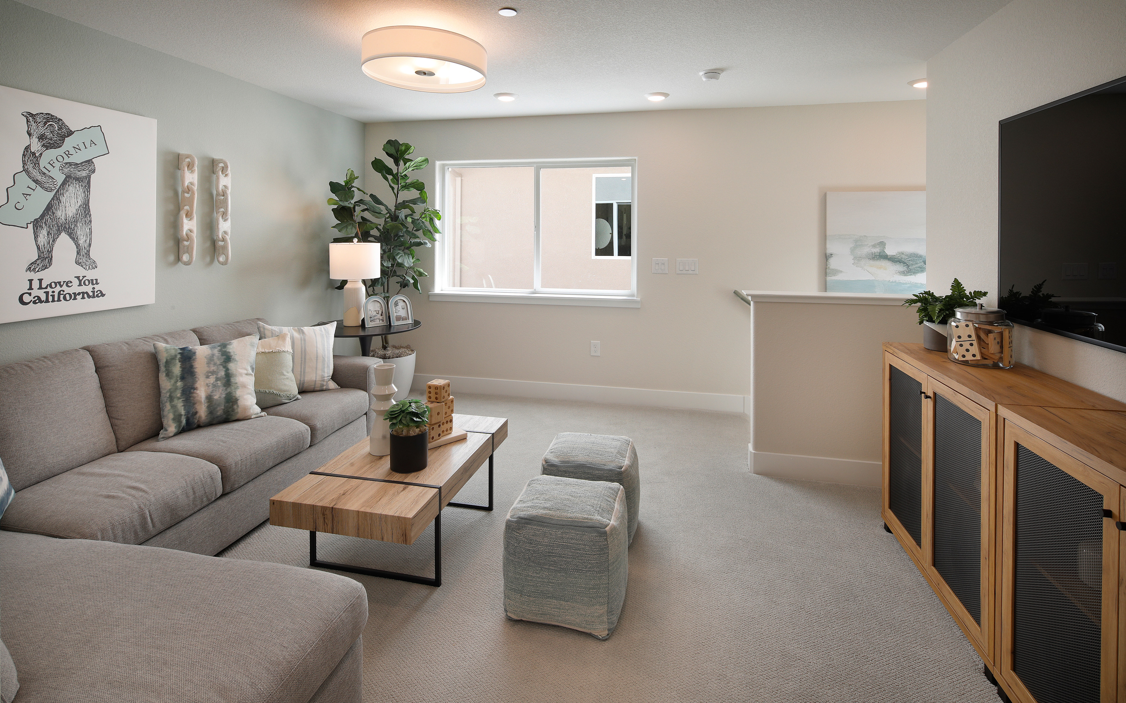 A cozy and inviting living room with a gray sectional sofa, a wooden coffee table, and various decorative elements such as plants and artwork on the walls.