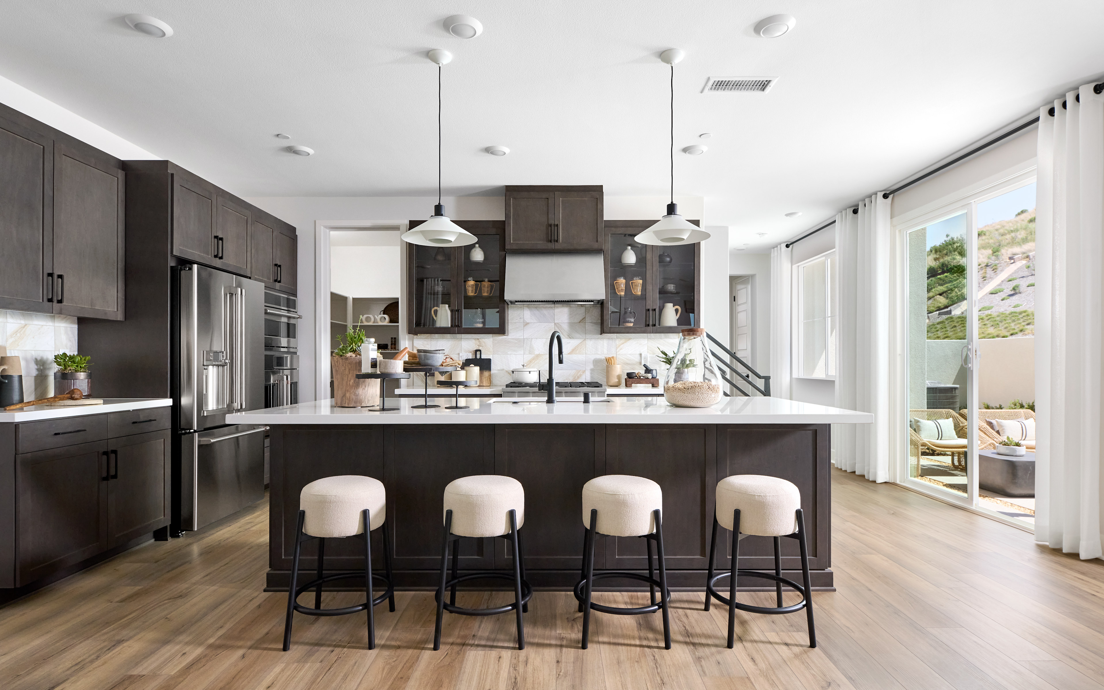 A modern and sleek kitchen with dark cabinets, a large island with bar stools, and a bright and airy atmosphere with large windows.