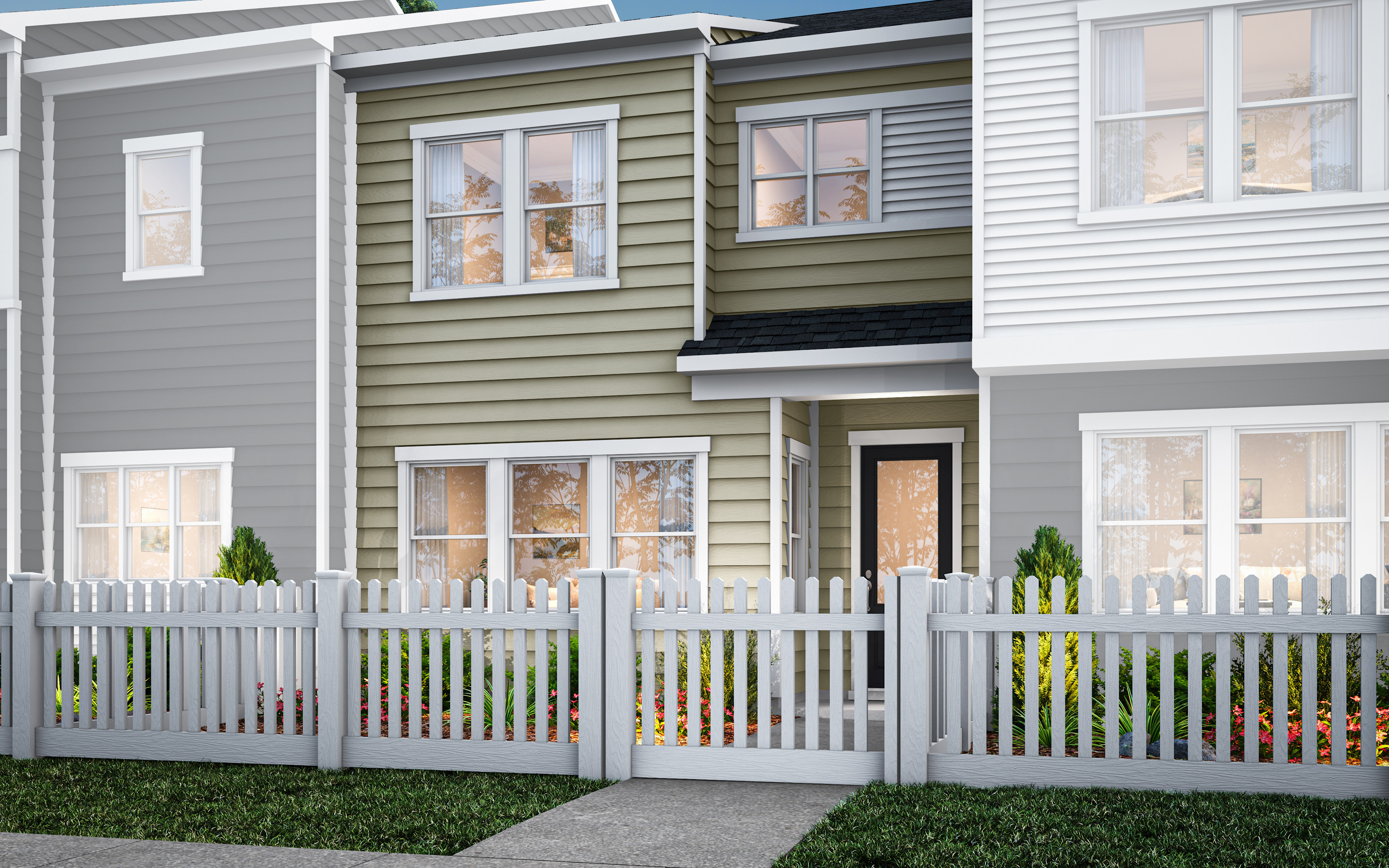A row of modern, multi-story townhouses with gray and green siding, white trim, and a white picket fence in the foreground, set against a clear blue sky.