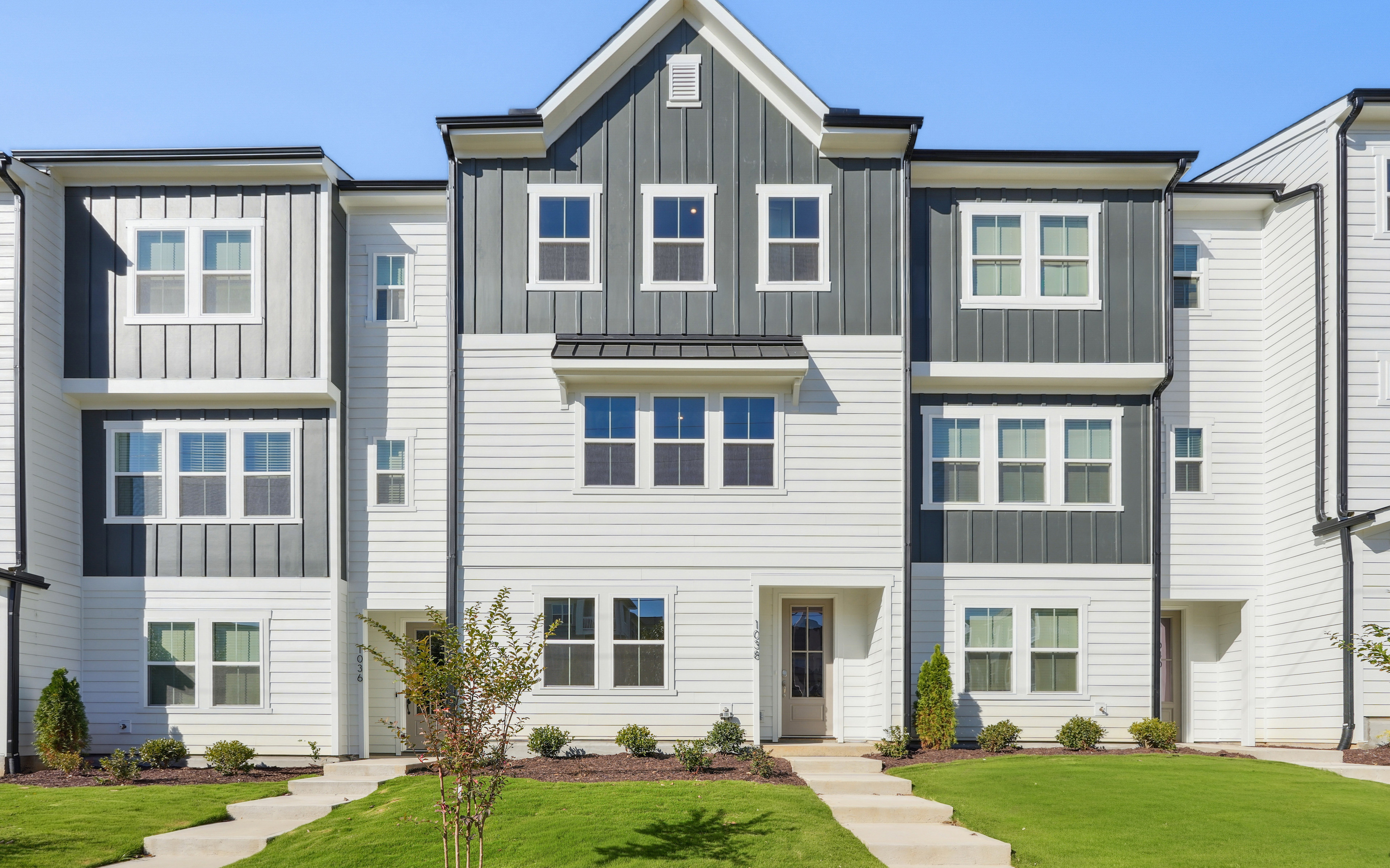 A multi-story residential building with a gray and white exterior, surrounded by a well-manicured lawn and landscaping.