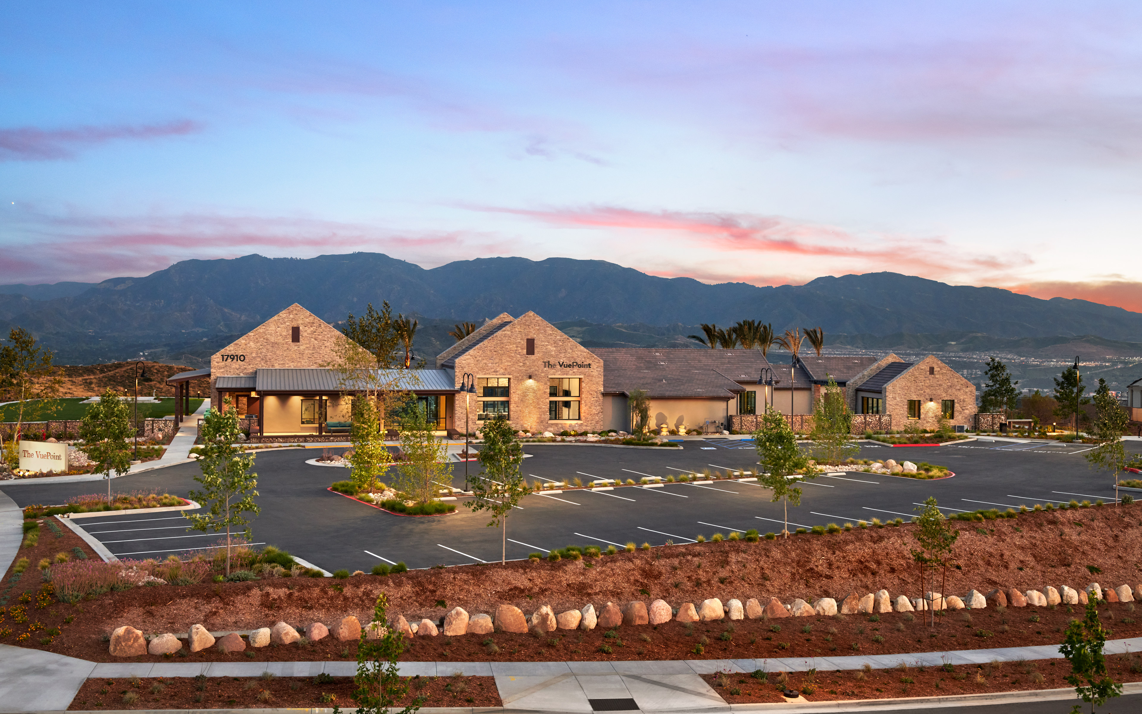 A residential community nestled against a backdrop of majestic mountains, with a well-landscaped parking lot in the foreground.