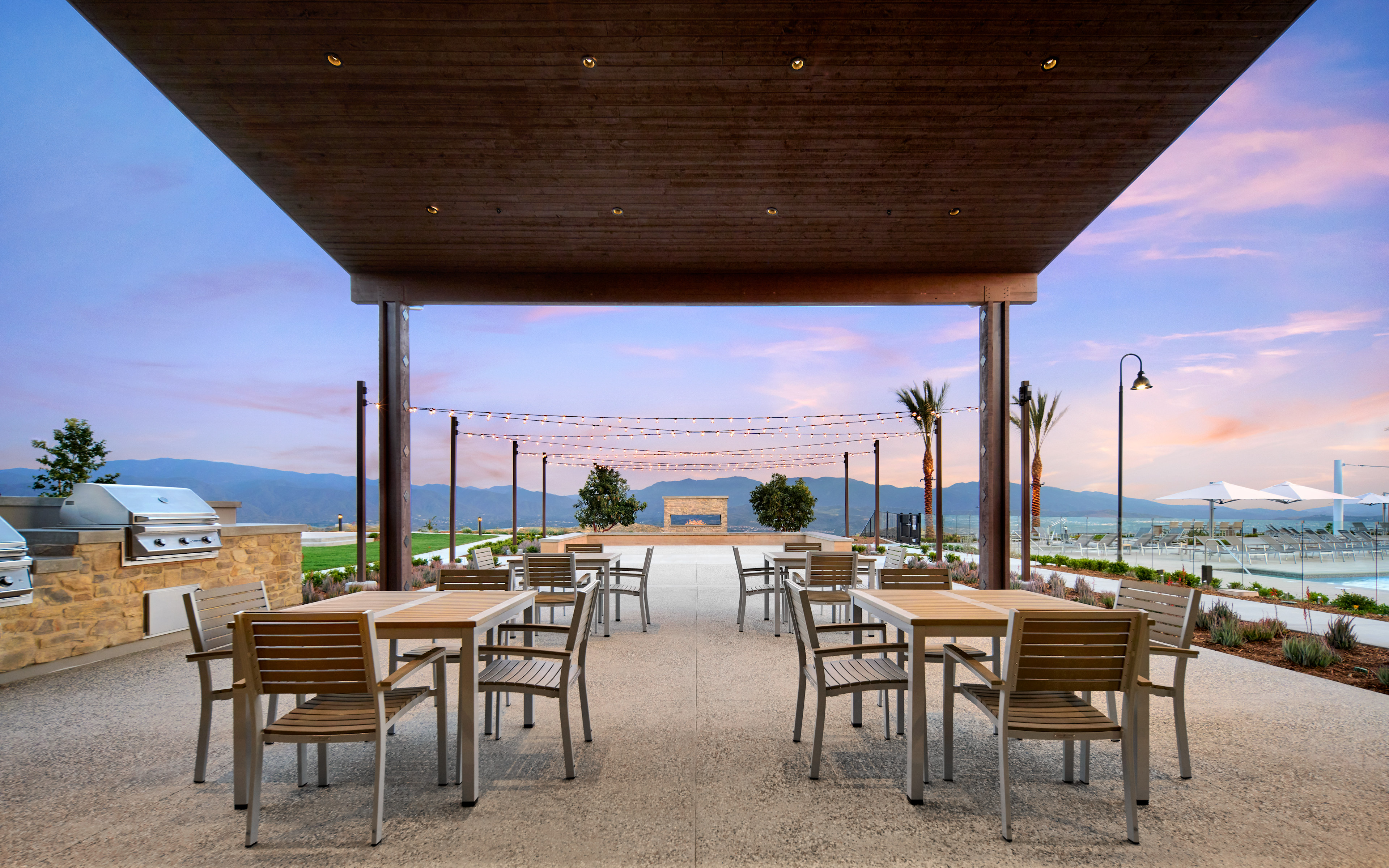 A covered outdoor dining area with wooden tables and chairs, overlooking a scenic landscape with mountains and a body of water in the background.