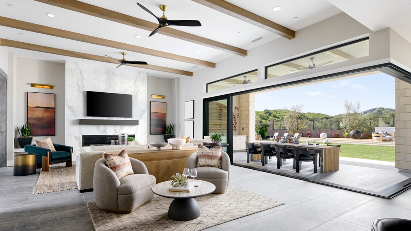A modern and spacious living room with a cozy seating area, a dining table, and large windows overlooking a lush outdoor landscape.