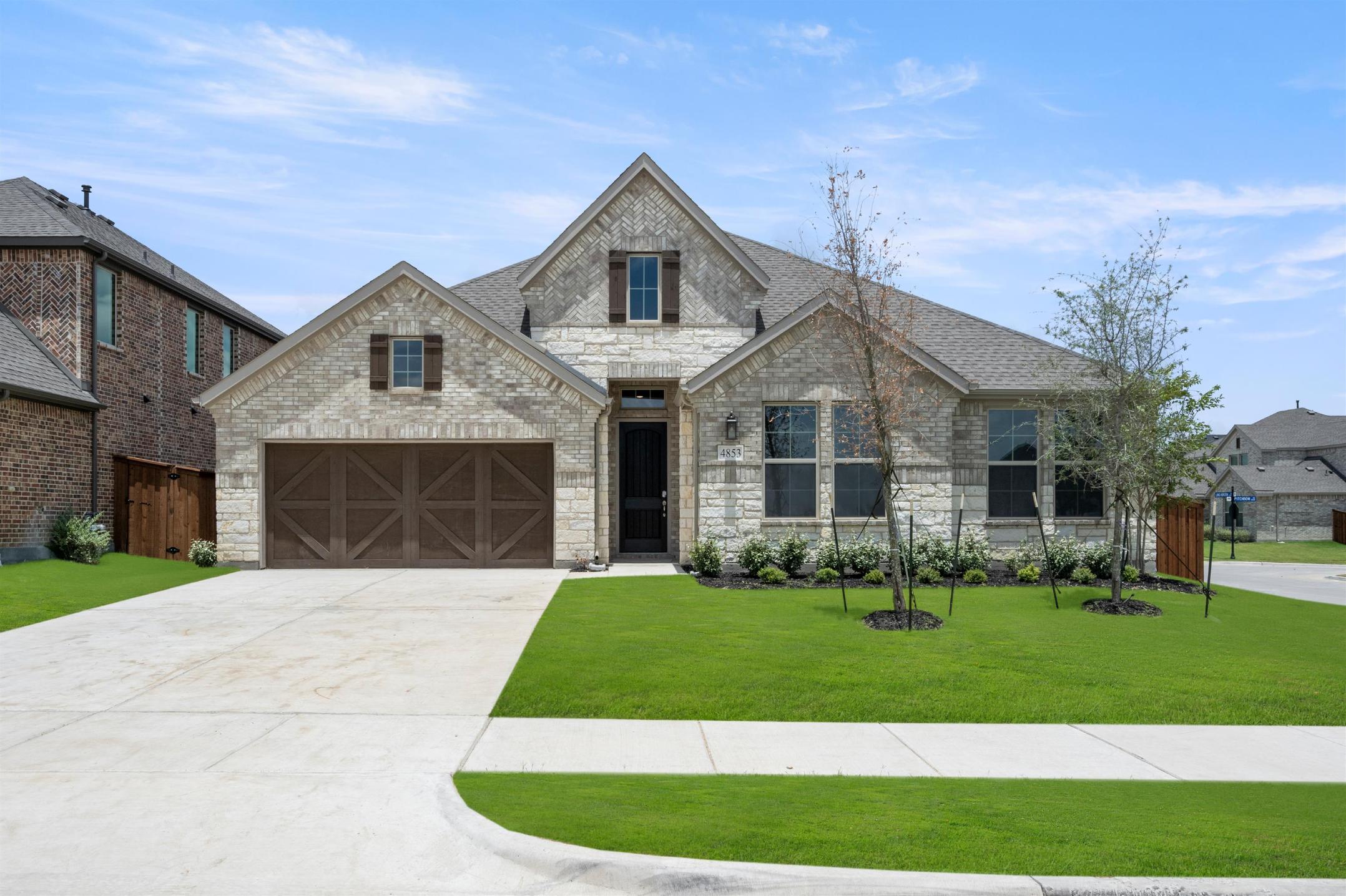 A two-story brick house with a gabled roof, surrounded by a well-manicured lawn and landscaping, set against a clear blue sky with scattered clouds.