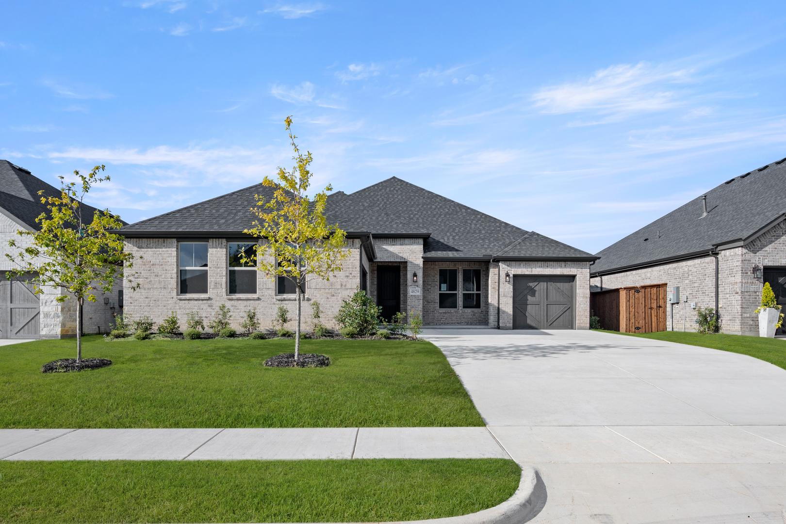 A modern, two-story house with a gray roof and exterior, surrounded by a well-manicured lawn and landscaping, set against a clear blue sky with scattered clouds.