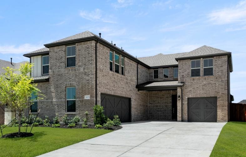 A large, modern brick house with a two-car garage, surrounded by a well-manicured lawn and landscaping, set against a clear blue sky with scattered clouds.