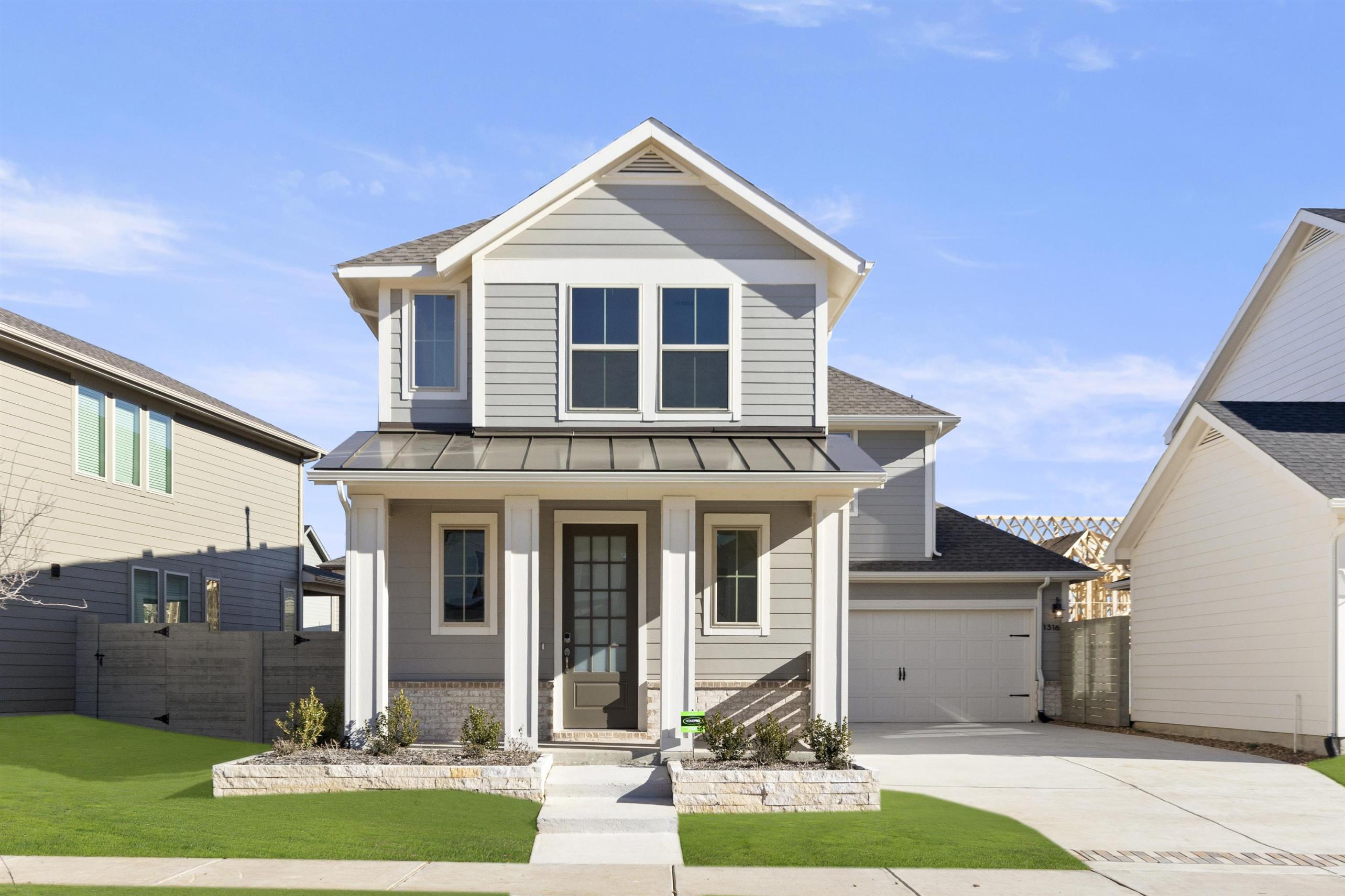 A two-story house with a gabled roof, white siding, and a covered porch stands in a well-manicured yard with a grassy lawn and a paved driveway leading to the street.