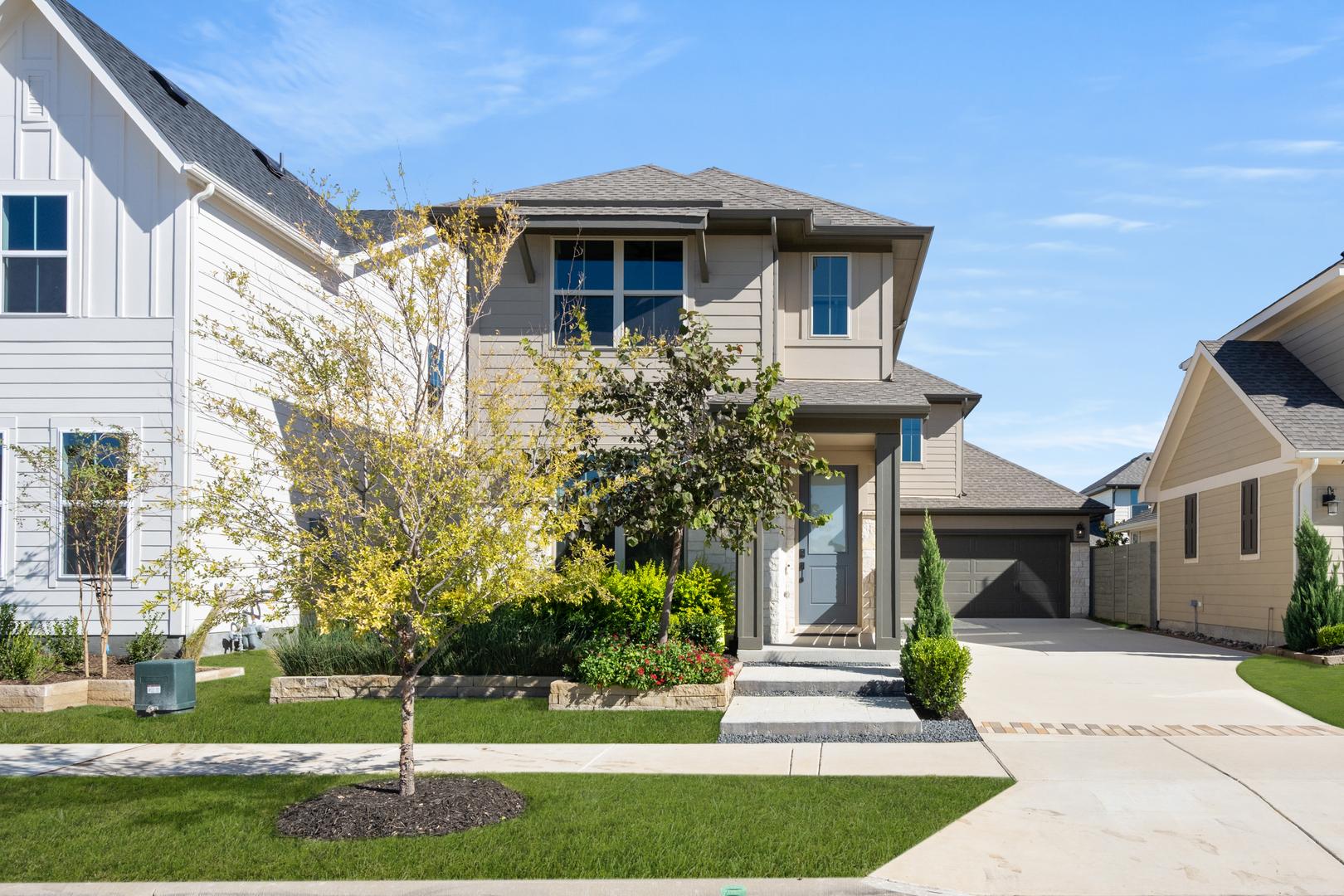A modern, two-story residential house with a well-manicured lawn, surrounded by other similar houses in a suburban neighborhood.