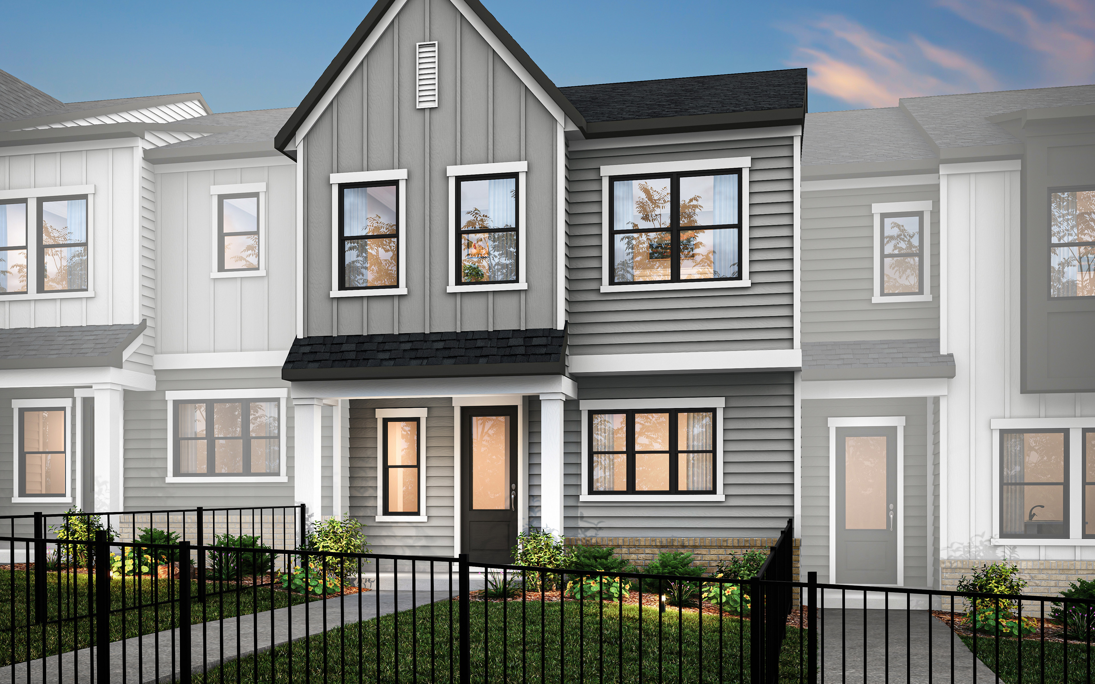 A modern, two-story townhouse with a gray exterior, black roof, and a small front yard enclosed by a metal fence, set against a clear blue sky.