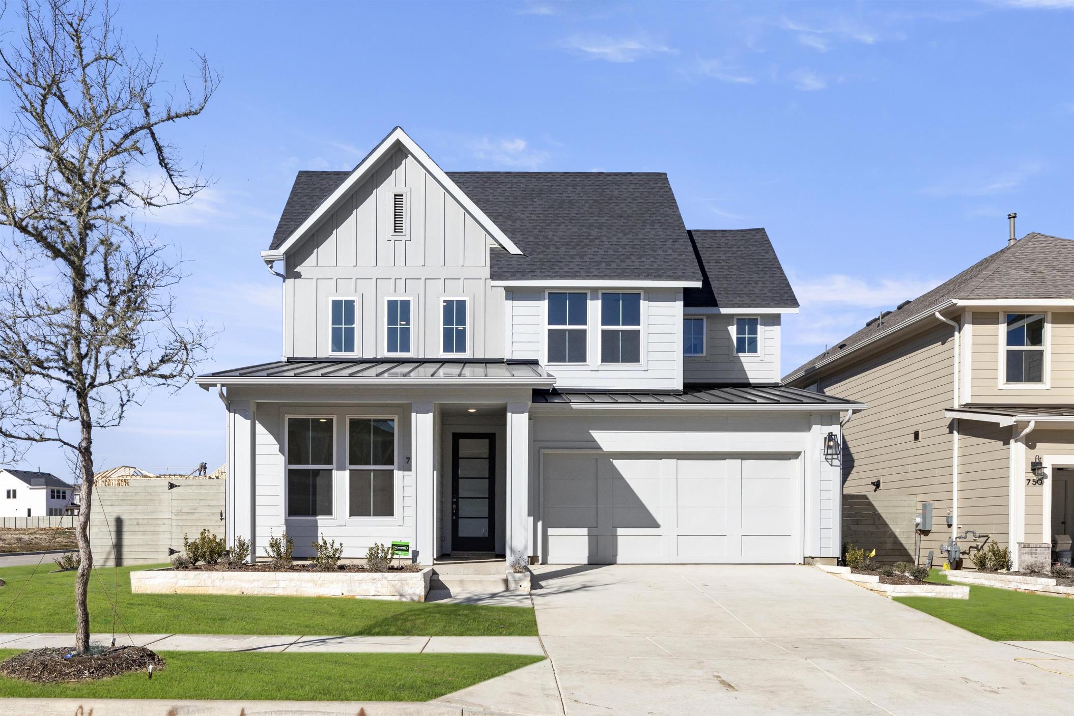 A modern two-story house with a white exterior, black roof, and a well-manicured lawn in the foreground, set against a clear blue sky.