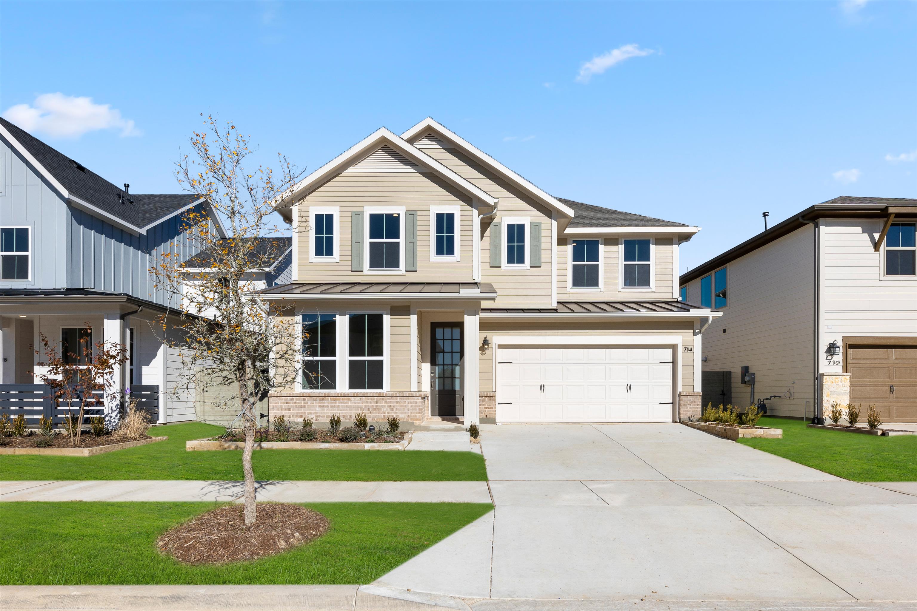 A two-story residential house with a garage, surrounded by a well-manicured lawn and landscaping, set against a clear blue sky with some clouds.