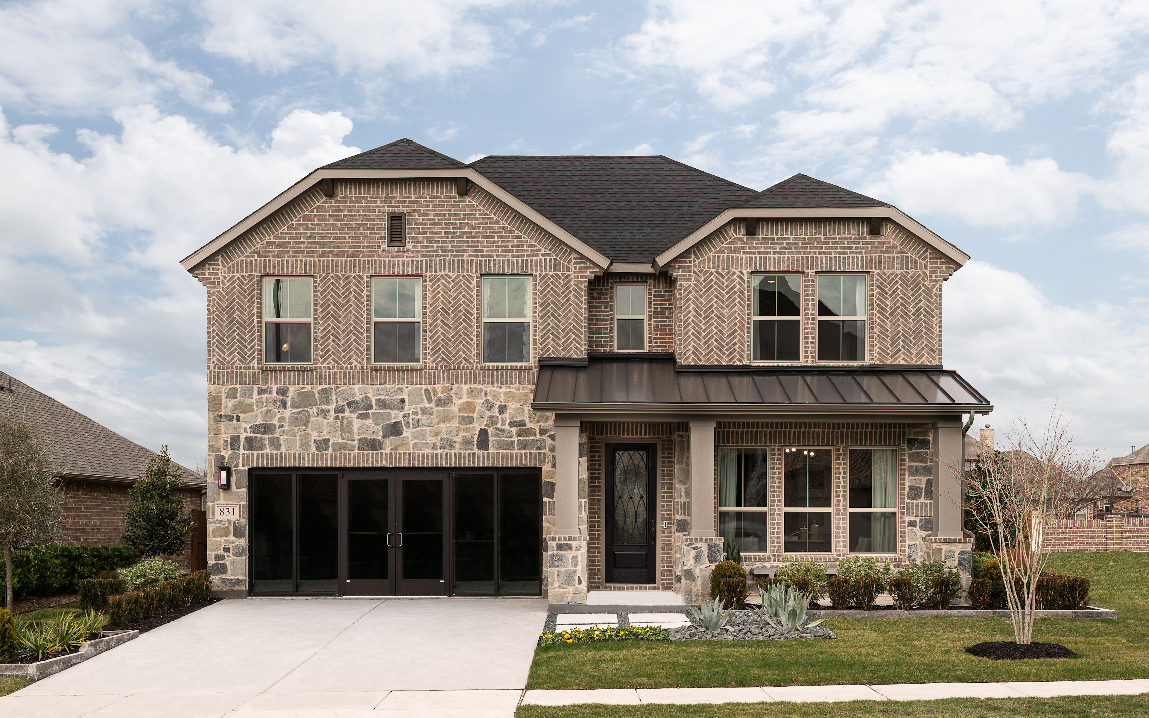 A two-story brick and stone house with a gabled roof, surrounded by a well-manicured lawn and landscaping, set against a cloudy sky.