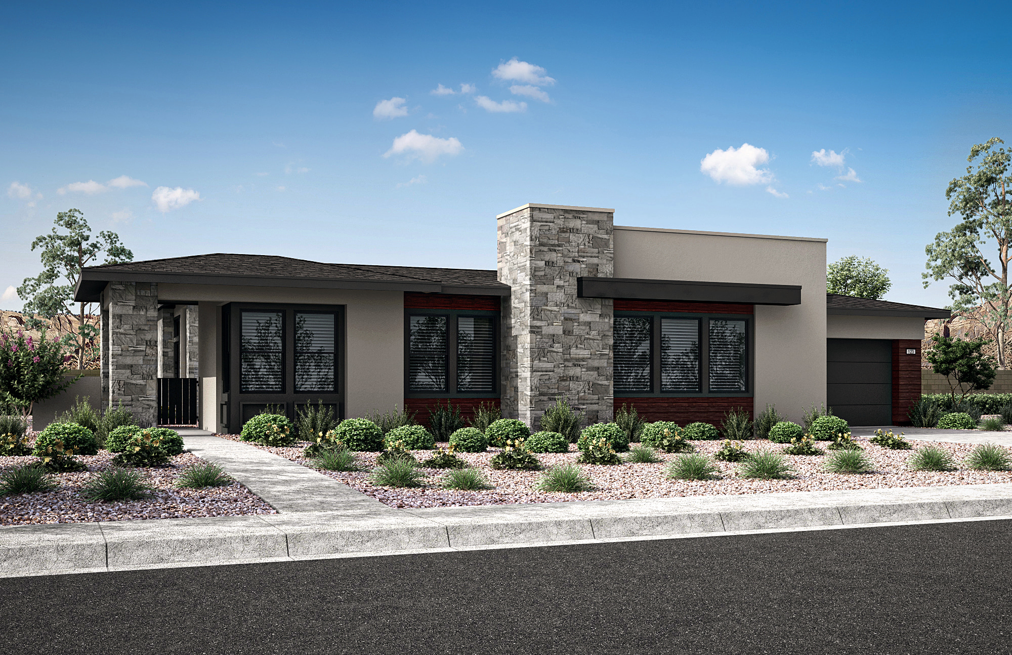 A modern, single-story house with a stone exterior, large windows, and a well-landscaped front yard featuring shrubs and a paved driveway, set against a clear blue sky with scattered clouds.