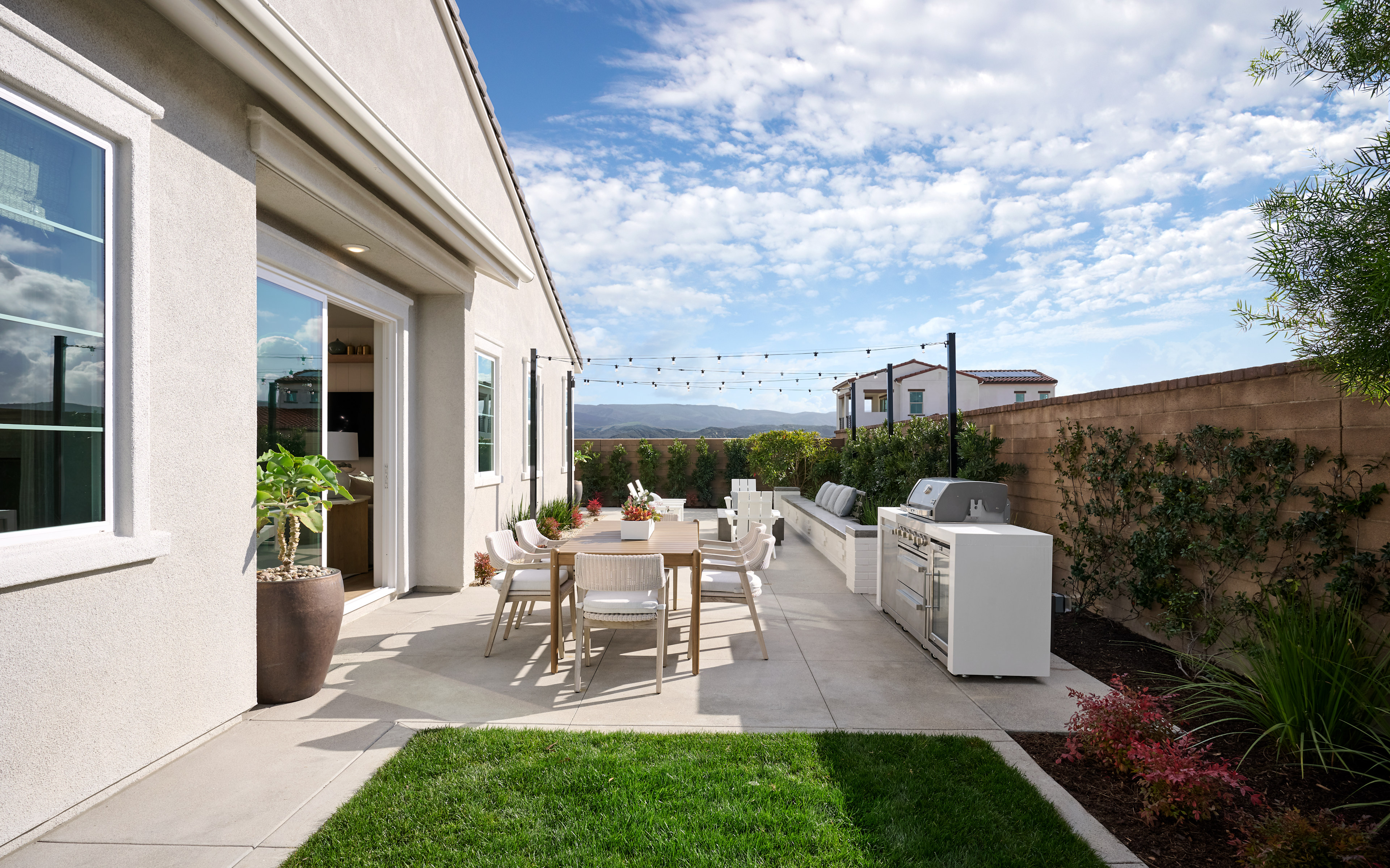 A well-designed outdoor living space with a patio, dining area, and landscaping, set against a backdrop of a clear blue sky with fluffy clouds.