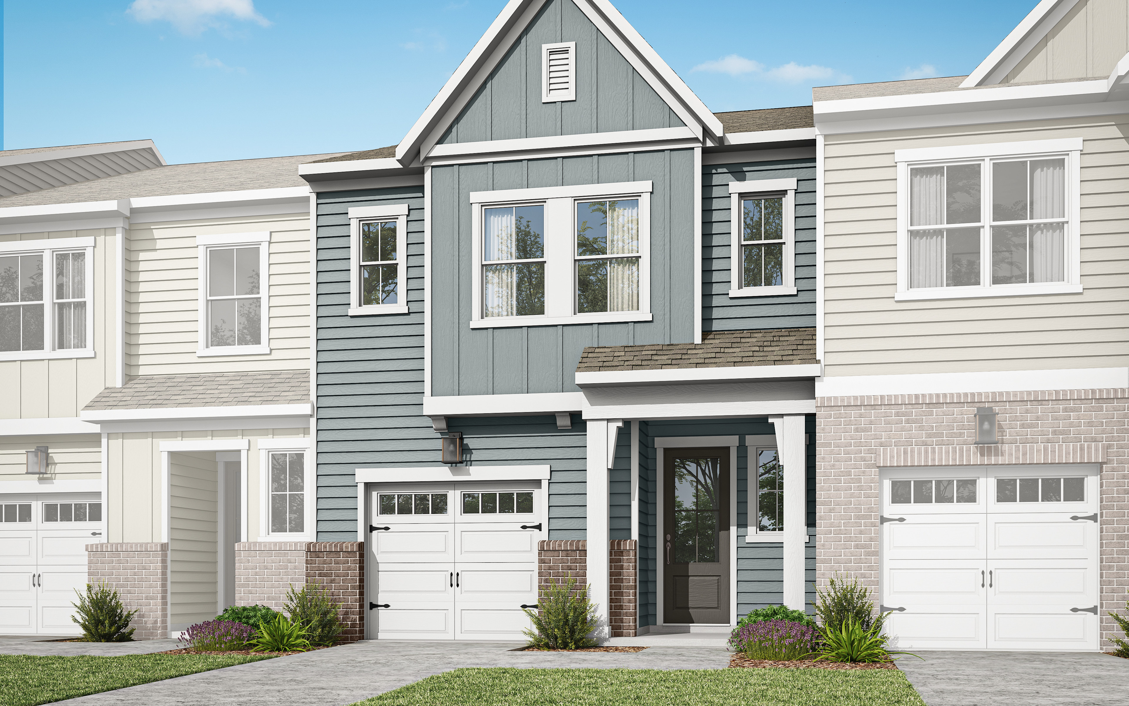 A modern, two-story townhouse with a gray exterior, white trim, and a prominent gable roof stands in a well-manicured yard with lush greenery in the foreground against a clear blue sky.