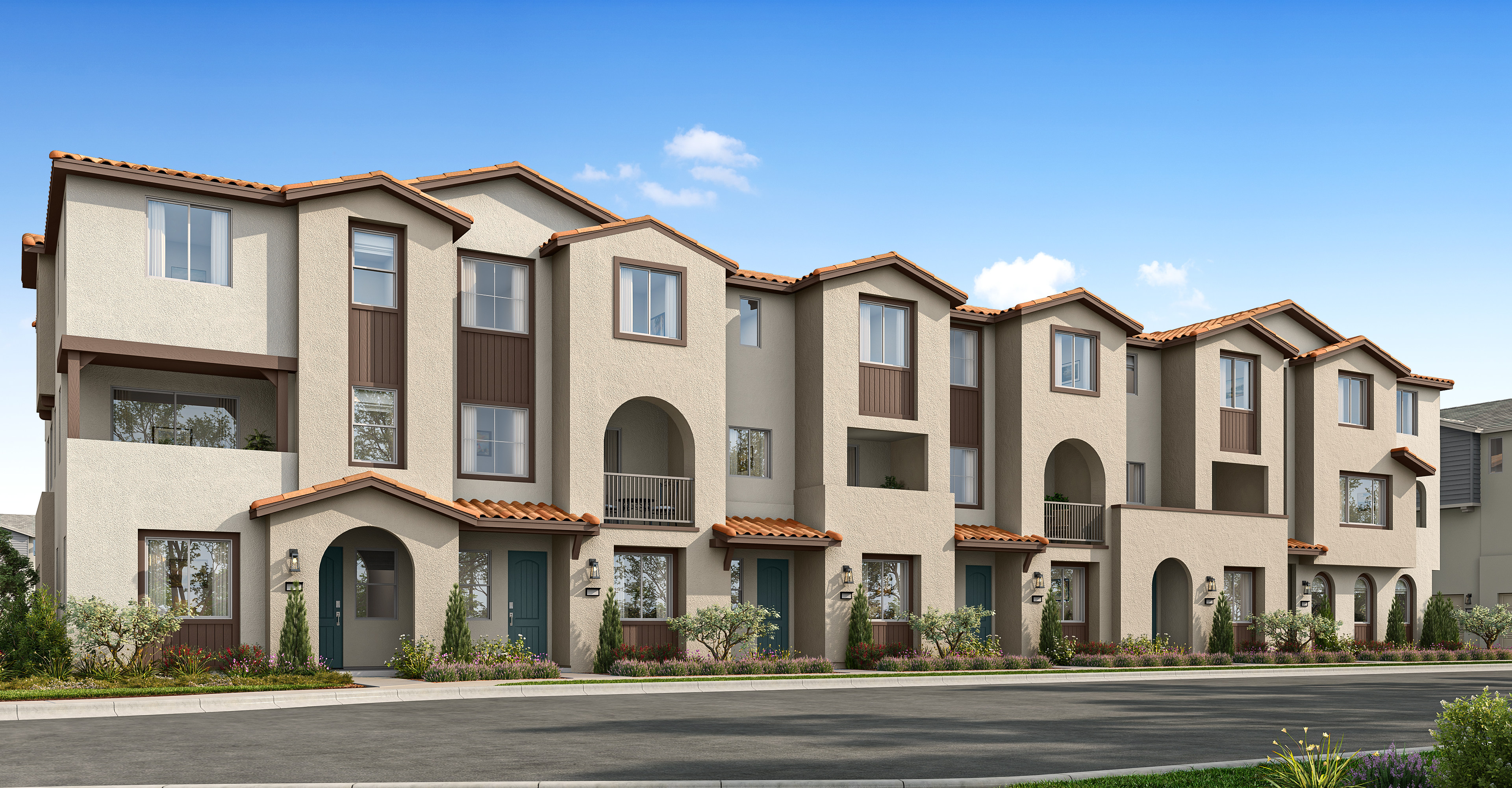 A row of multi-story townhouses with a mix of beige and brown exterior colors, set against a clear blue sky in the background.