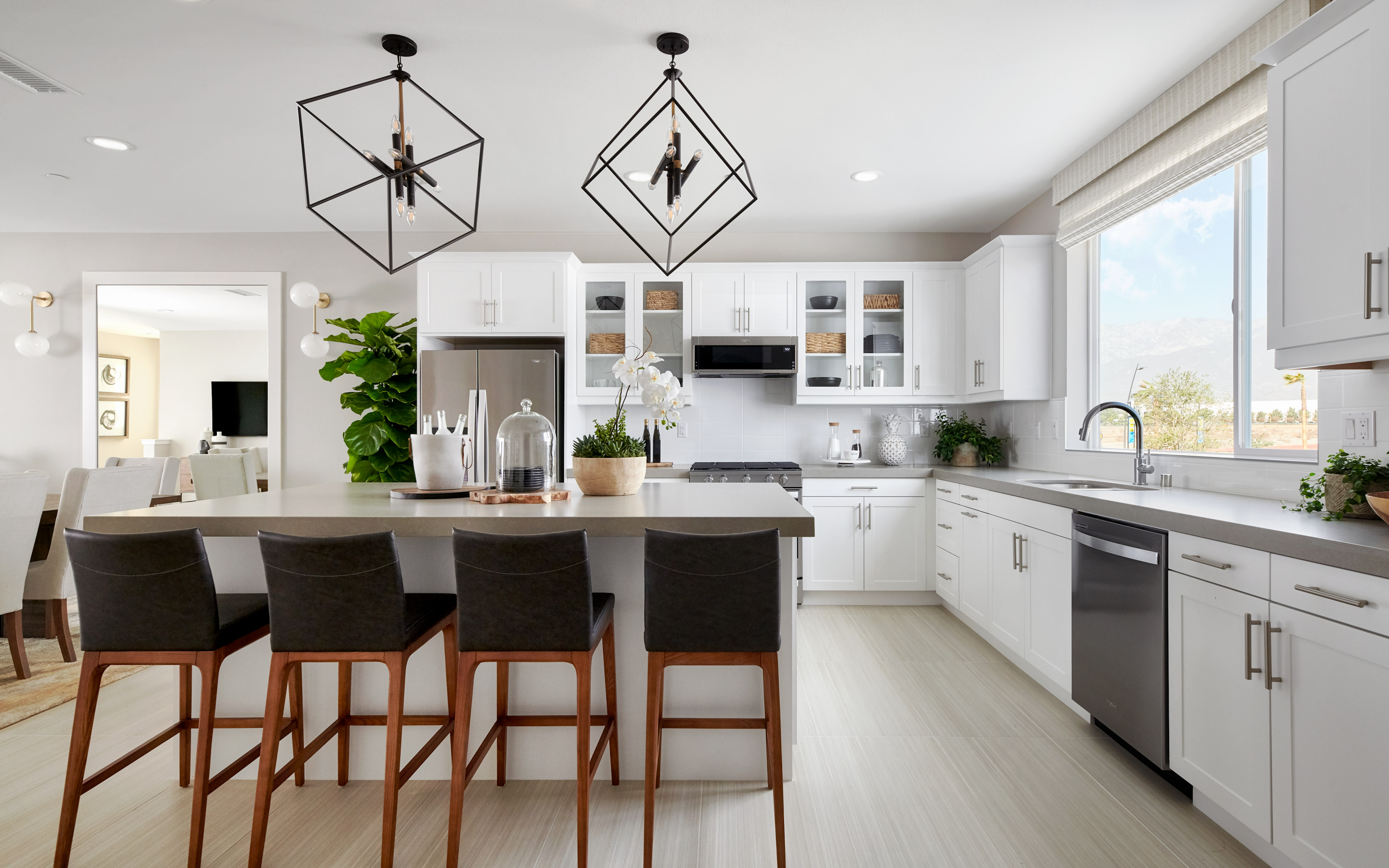 A modern, open-concept kitchen with white cabinets, stainless steel appliances, and a large island with bar stools, complemented by stylish pendant lighting fixtures.