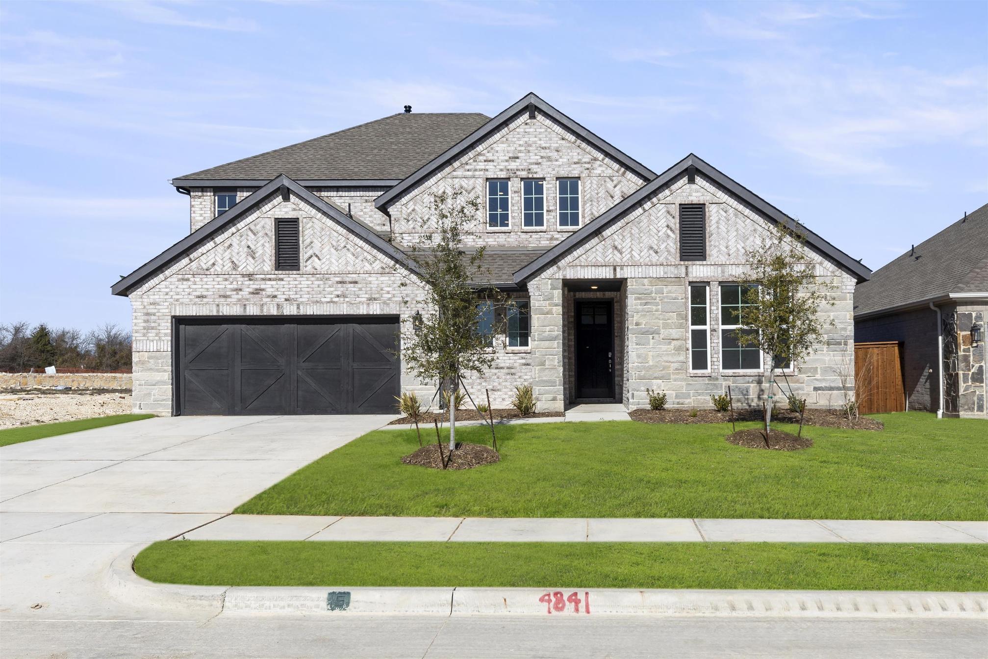 A two-story stone house with a garage, surrounded by a well-manicured lawn and situated in a residential neighborhood.