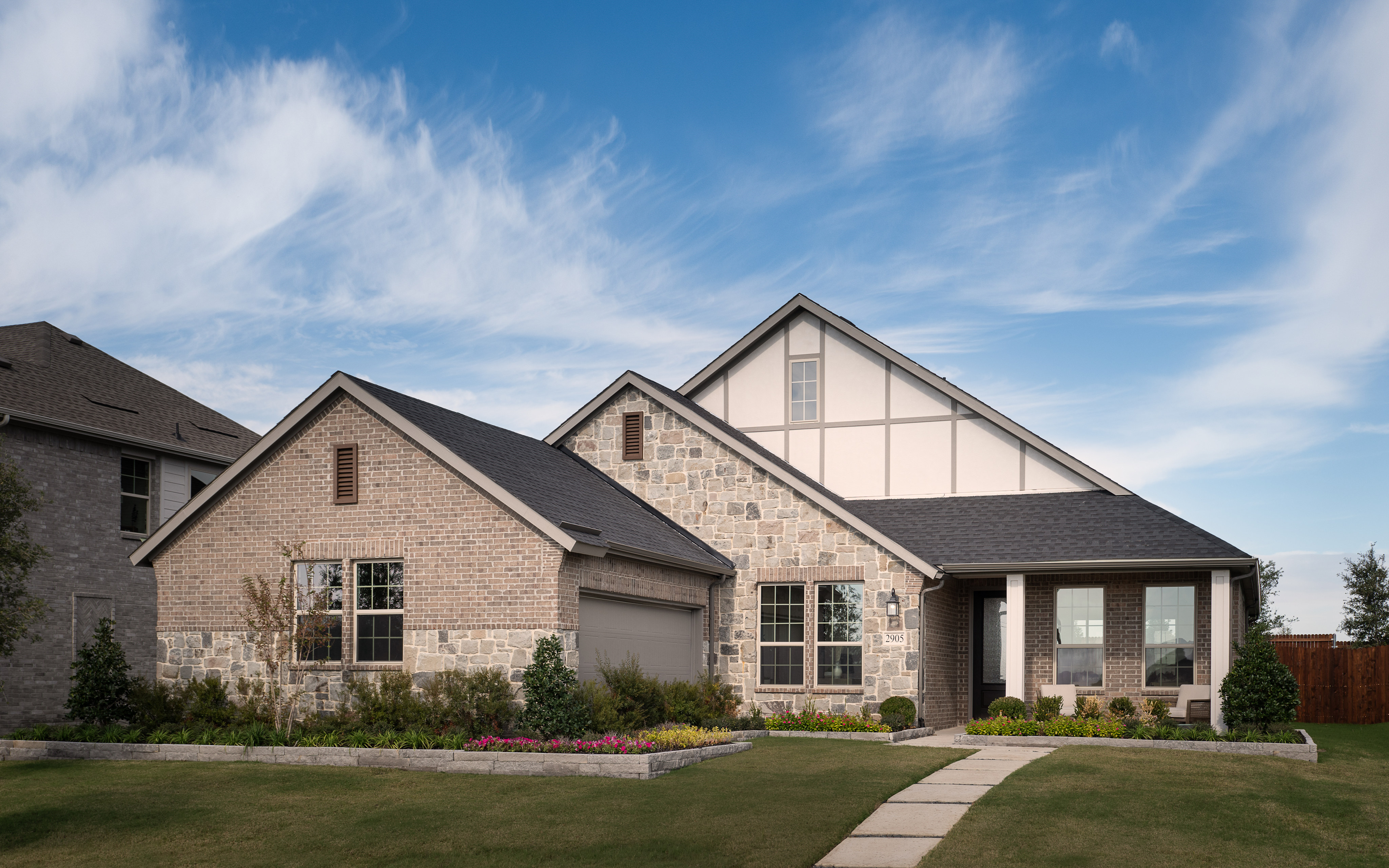 A two-story brick house with a gabled roof and a well-manicured lawn in the foreground, set against a blue sky with wispy clouds.