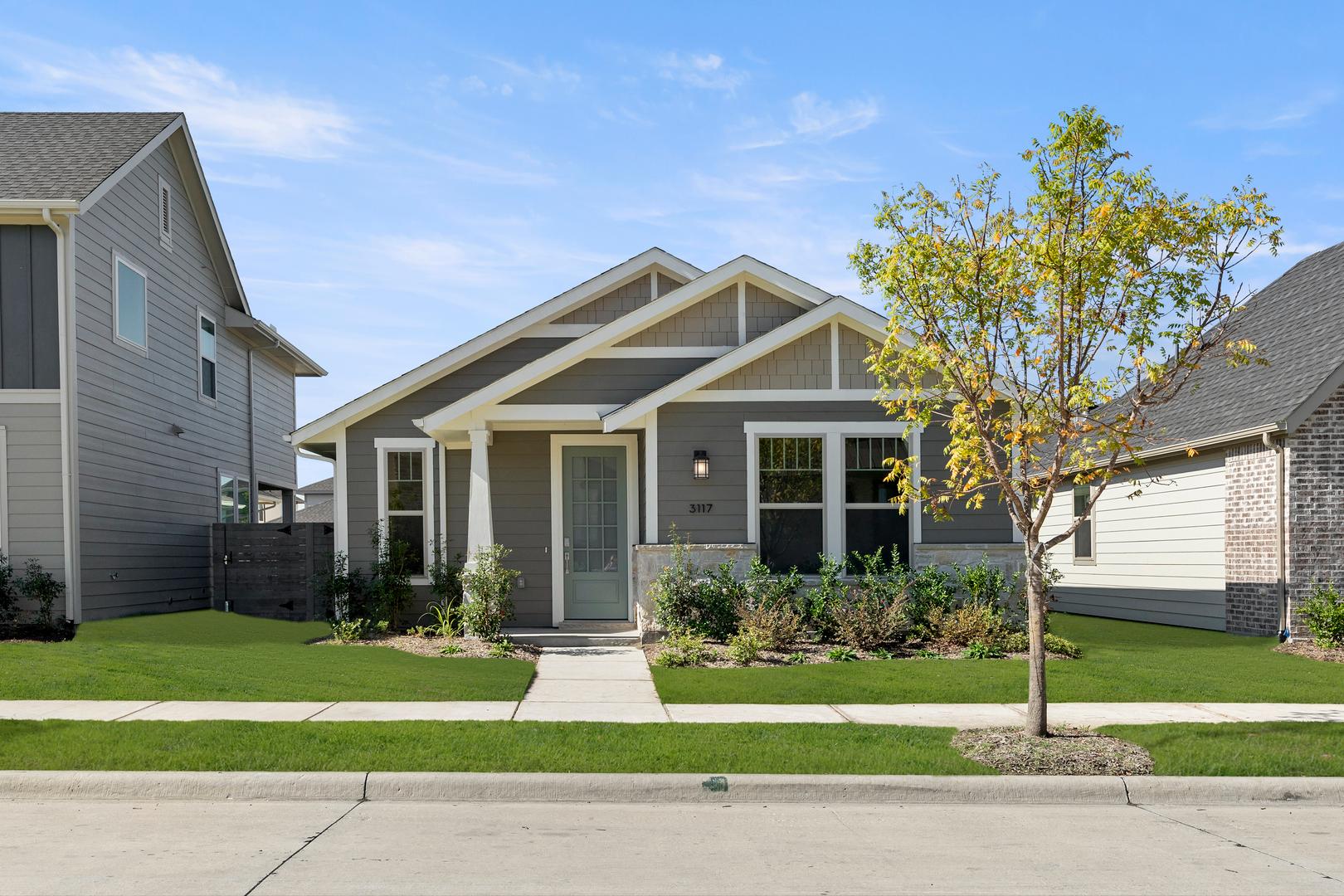 A well-maintained residential home with a neatly landscaped yard, surrounded by trees and a clear blue sky.