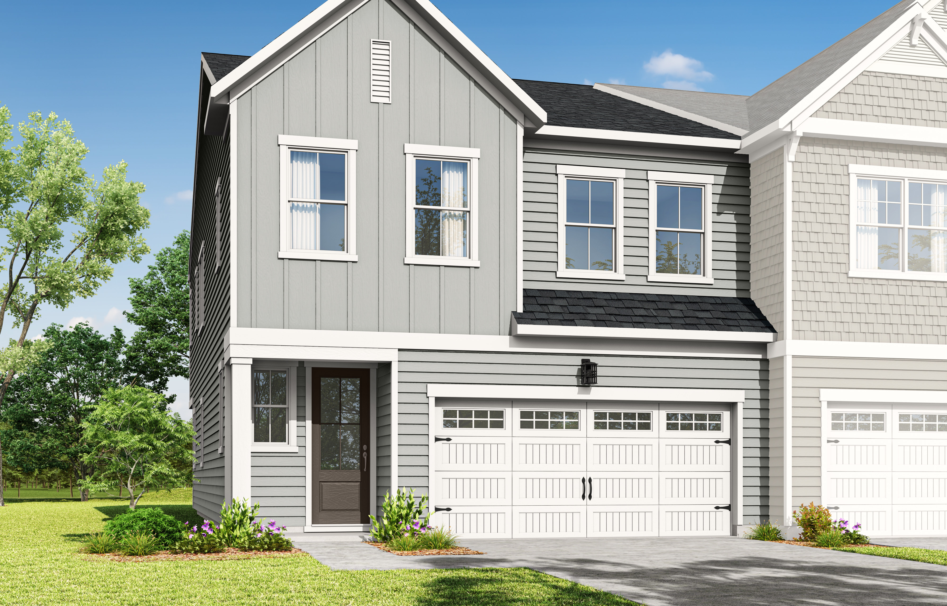 A two-story residential building with a gray exterior, white trim, and a garage door stands in a grassy area surrounded by trees.