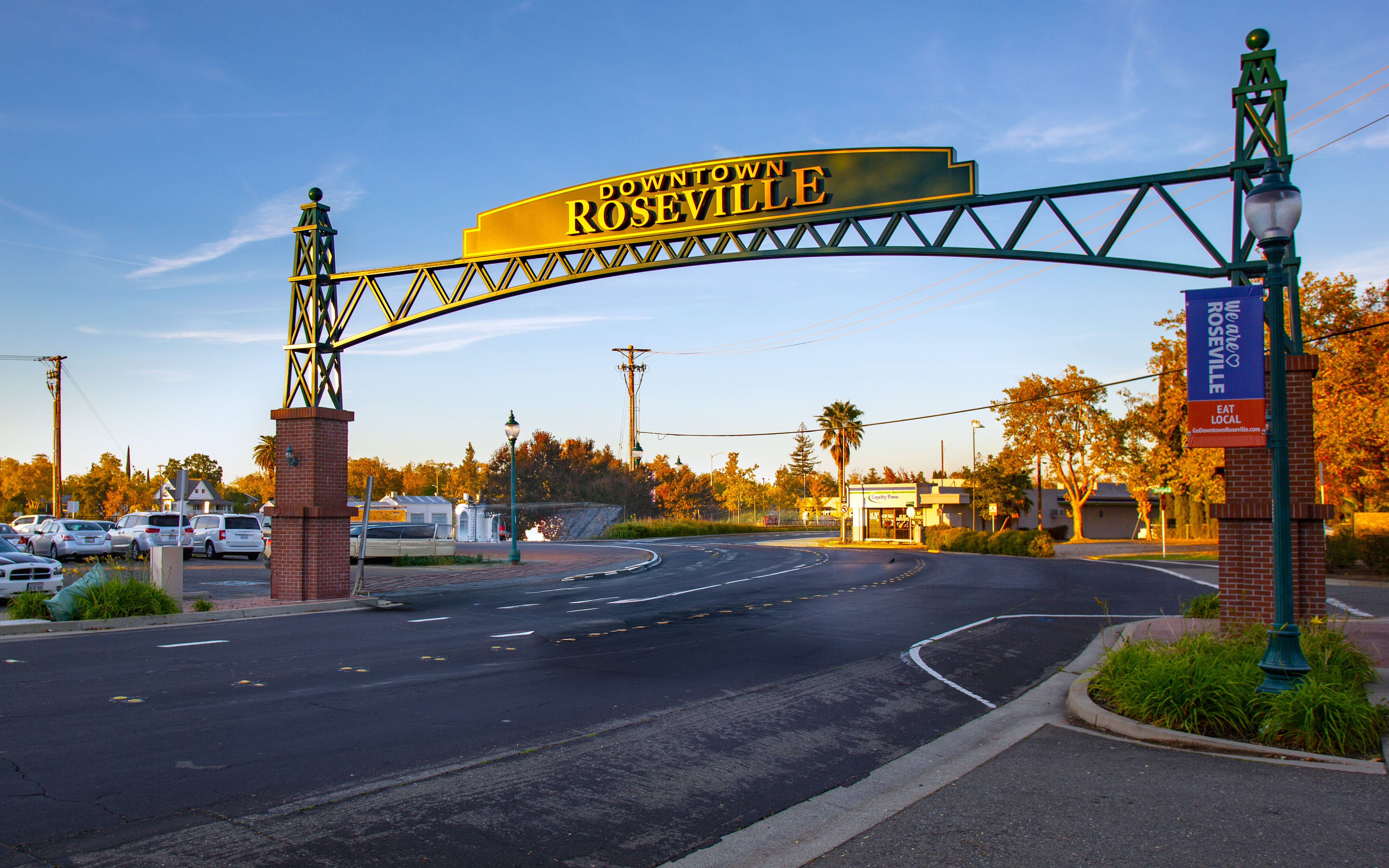 A large "Downtown Roseville" arch spans a paved road in the foreground, with trees and a clear blue sky in the background.
