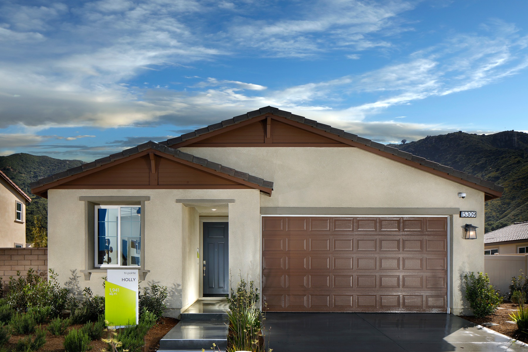 A single-story house with a wooden roof and a garage door stands in the foreground, surrounded by lush greenery and set against a backdrop of a blue sky with wispy clouds.